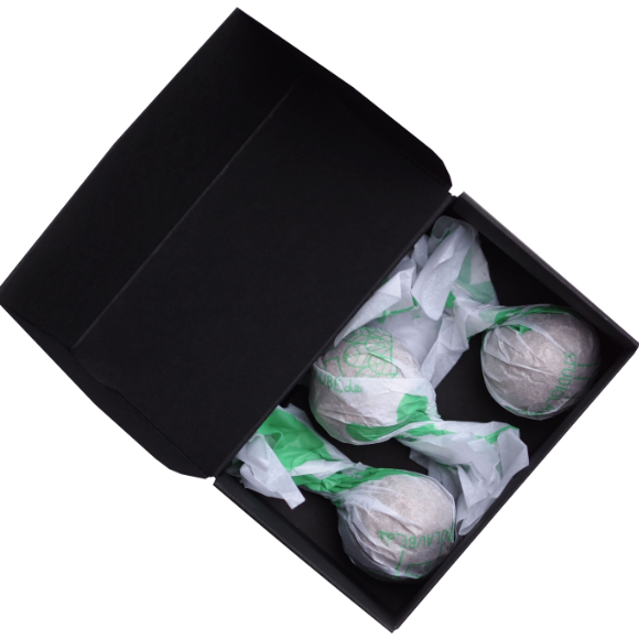 Eine schwarze Schachtel, die drei runde Gegenstände enthält, die in weißes und grünes Seidenpapier eingewickelt und teilweise ausgepackt sind, um ihre Formen zu enthüllen.