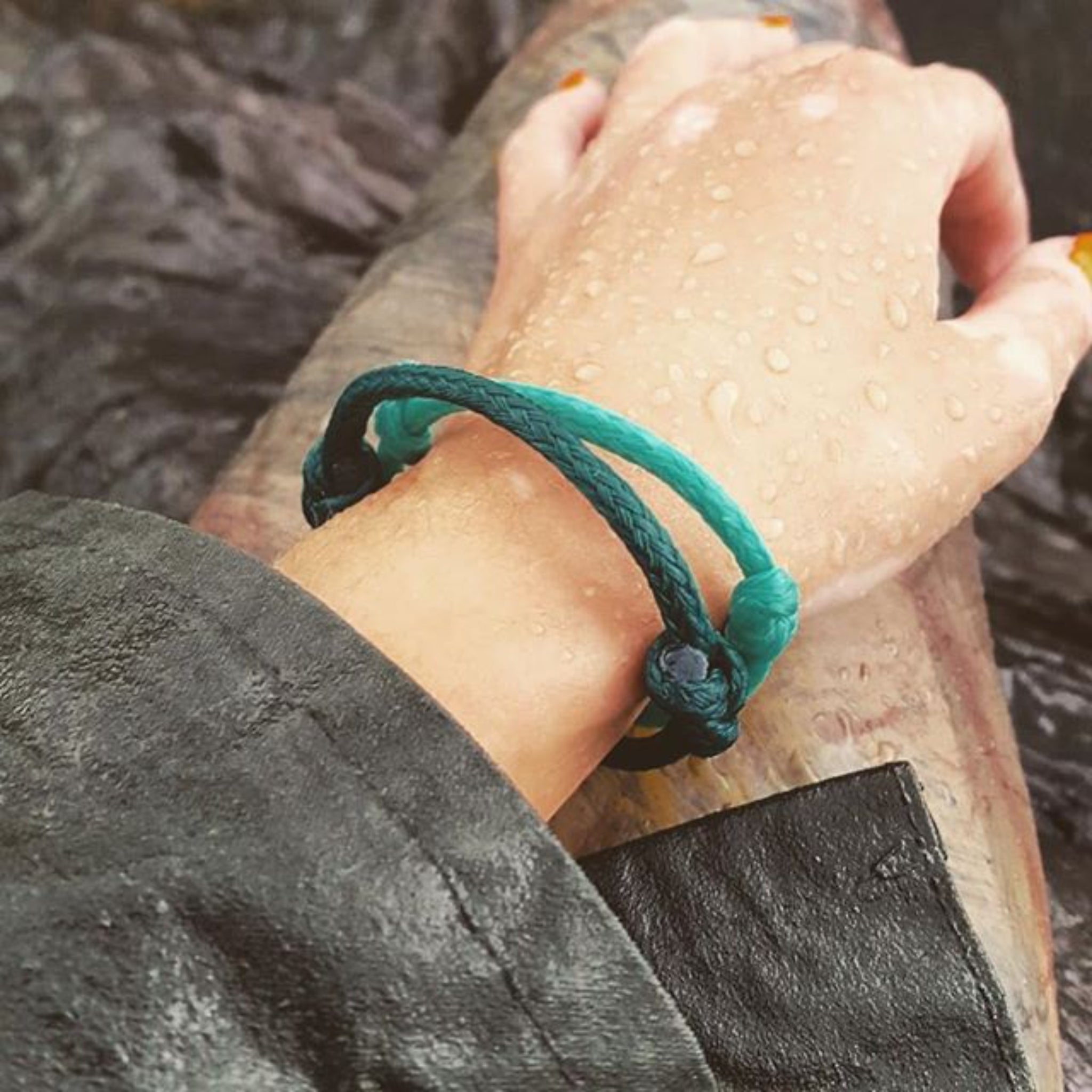 Hand mit grüner Armband und Wassertropfen auf einem nassen Ärmel.
