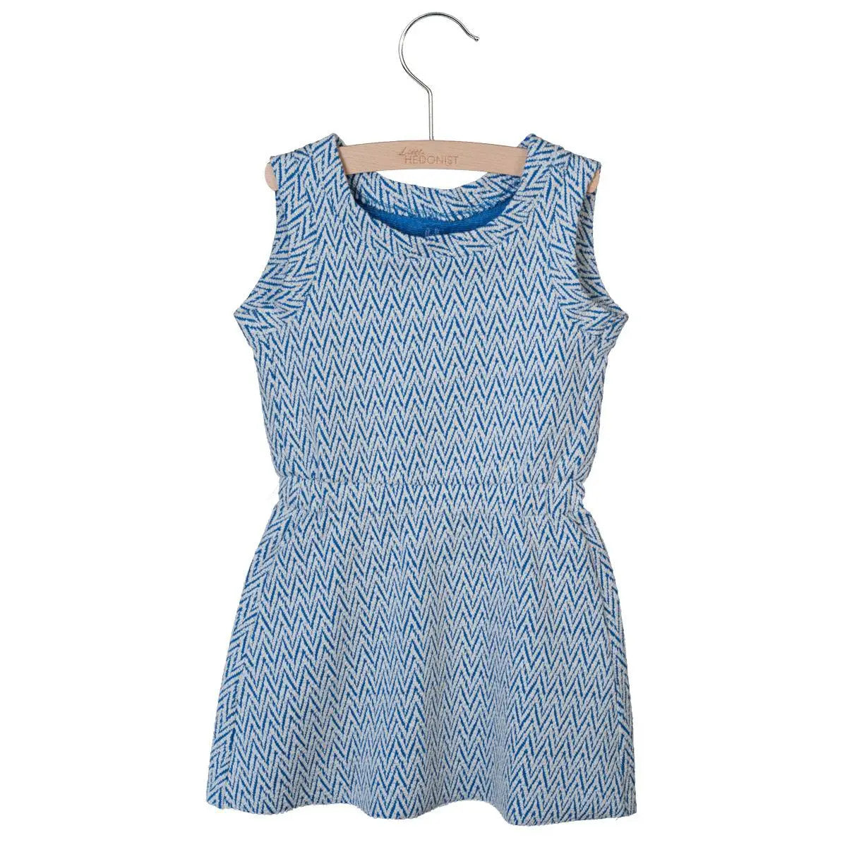 Ein ärmelloses, knielanges, blau-weißes Kleid mit Zickzackmuster, das in der Taille gerafft ist und auf einem Holzbügel vor weißem Hintergrund ausgestellt ist.
