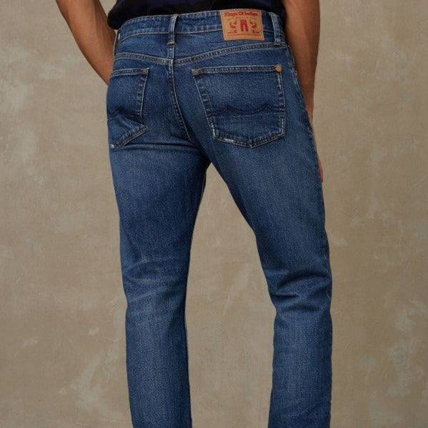 Person in blauer Jeans von hinten, vor einem neutralen Hintergrund stehend.