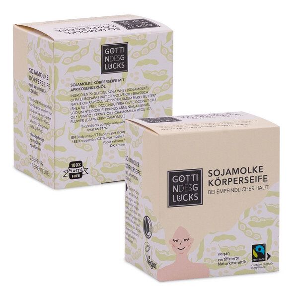 Zwei beigefarbene Schachteln der Seife Göttin des Glücks Sojamilch Körperseife mit minimalistischen grünen Blattmotiven und Logos, die auf die Veganer- und Fairtrade-Zertifizierung hinweisen, sowie einem deutschen Text zur Beschreibung des Produkts.