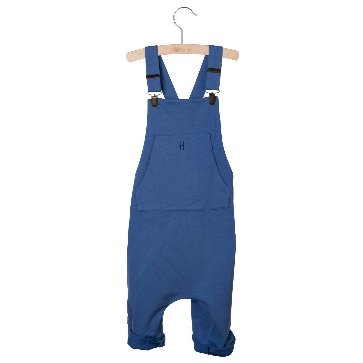 Blauer Kinderoverall mit verstellbaren Schulterträgern und einer Vordertasche, aufgehängt an einem Holzbügel vor weißem Hintergrund.