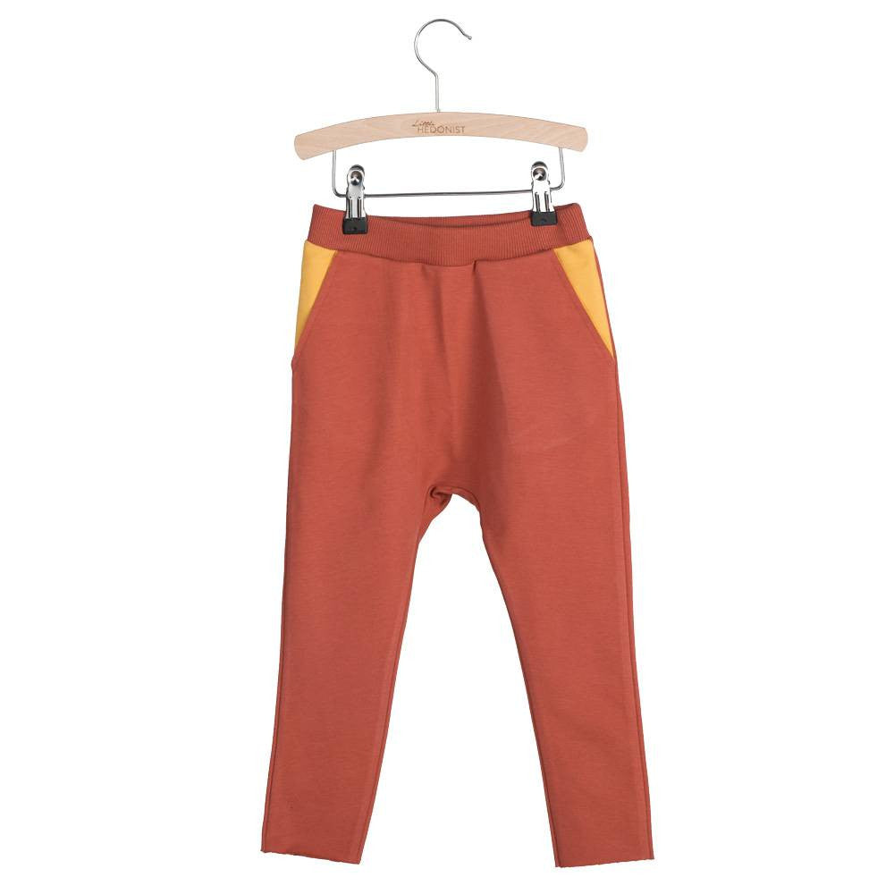 Rostfarbene Kinderhose mit gelben Taschen, ausgestellt auf einem Holzbügel vor weißem Hintergrund.