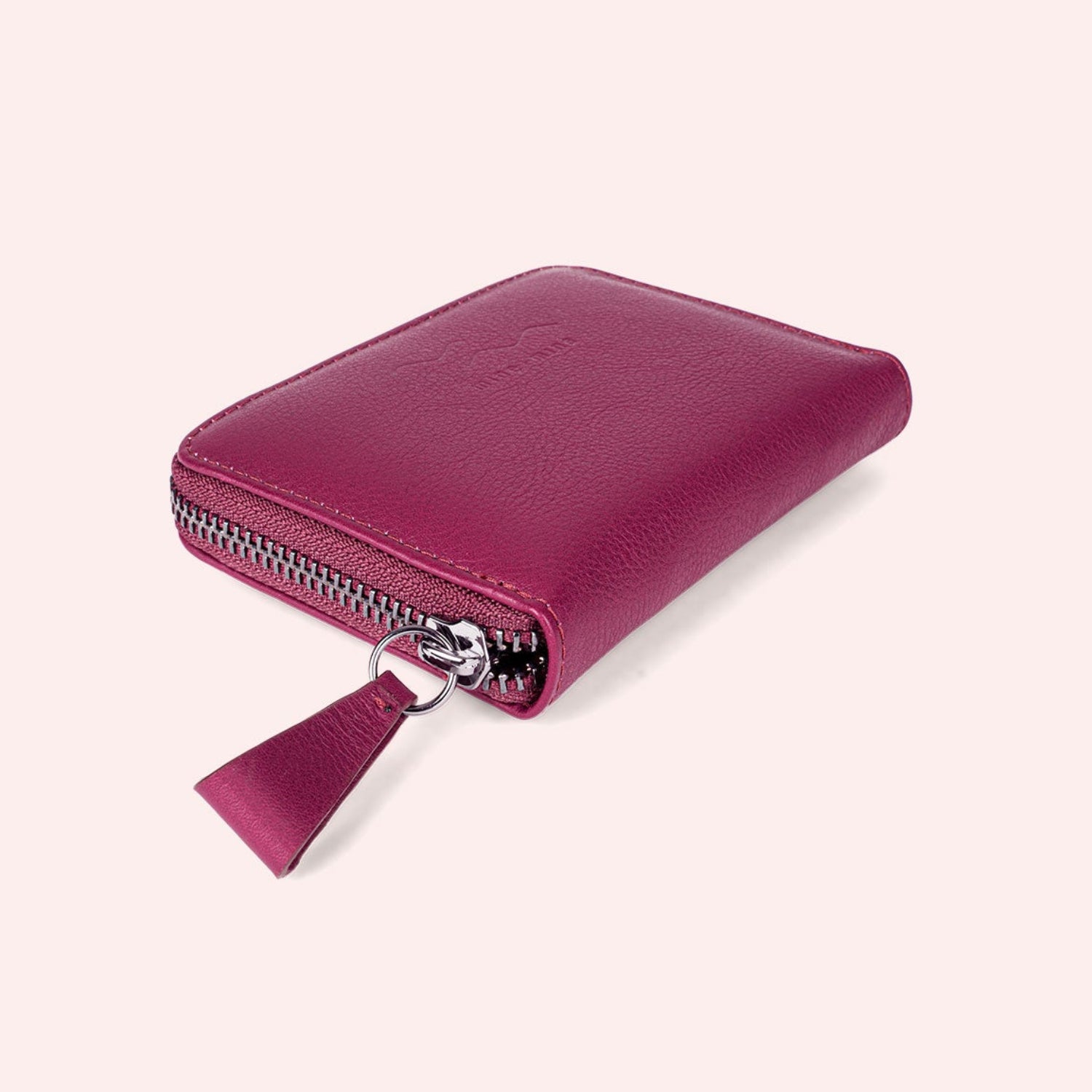 Ein kleines, quadratisches, rosa Lederportemonnaie mit silbernem Reißverschluss und passender Lederlasche auf einem schlichten, hellen Hintergrund.