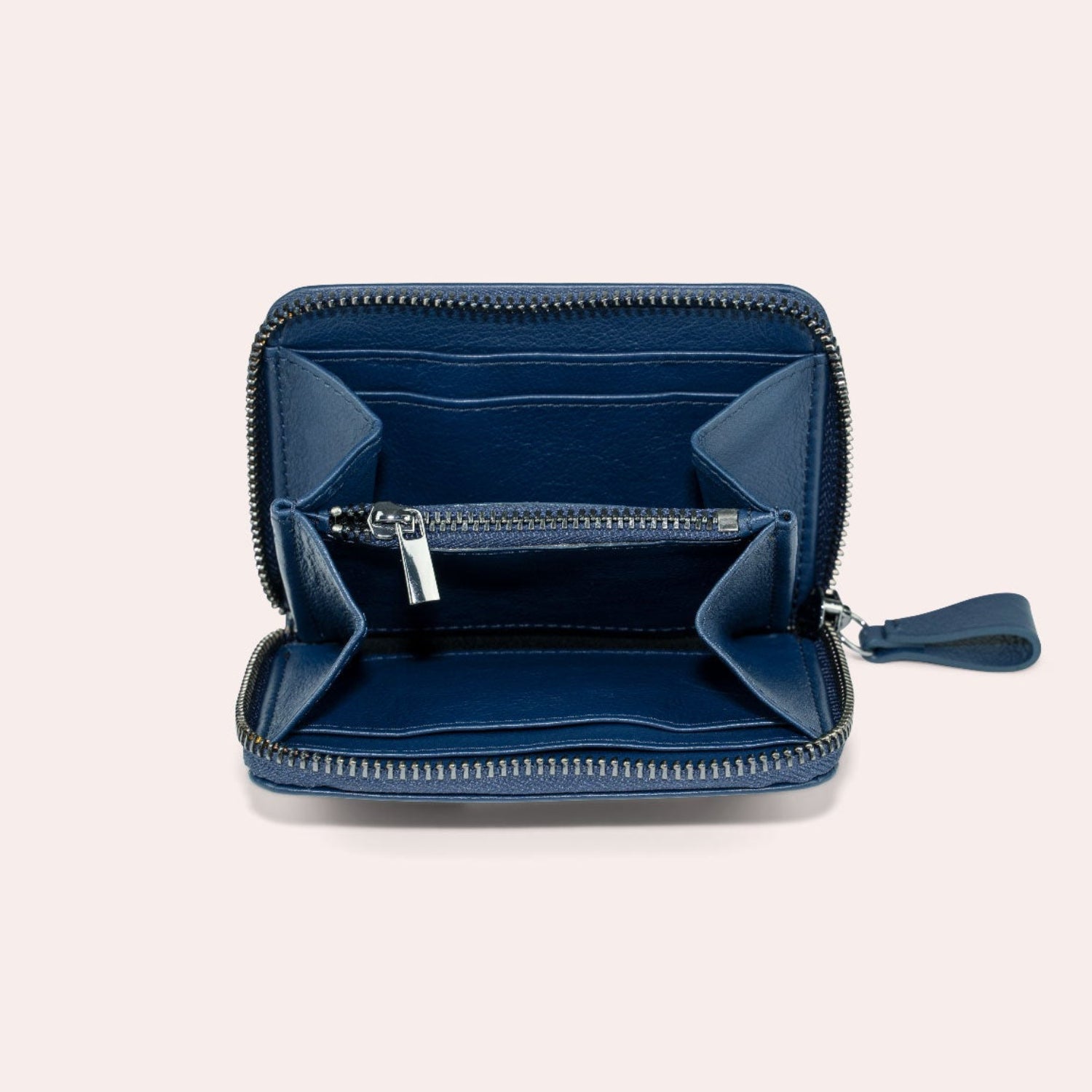 Eine kleine, marineblaue Brieftasche mit Reißverschluss mit mehreren Kartenfächern und einem Münzfach, die offen auf einem hellbeigen Hintergrund dargestellt wird.