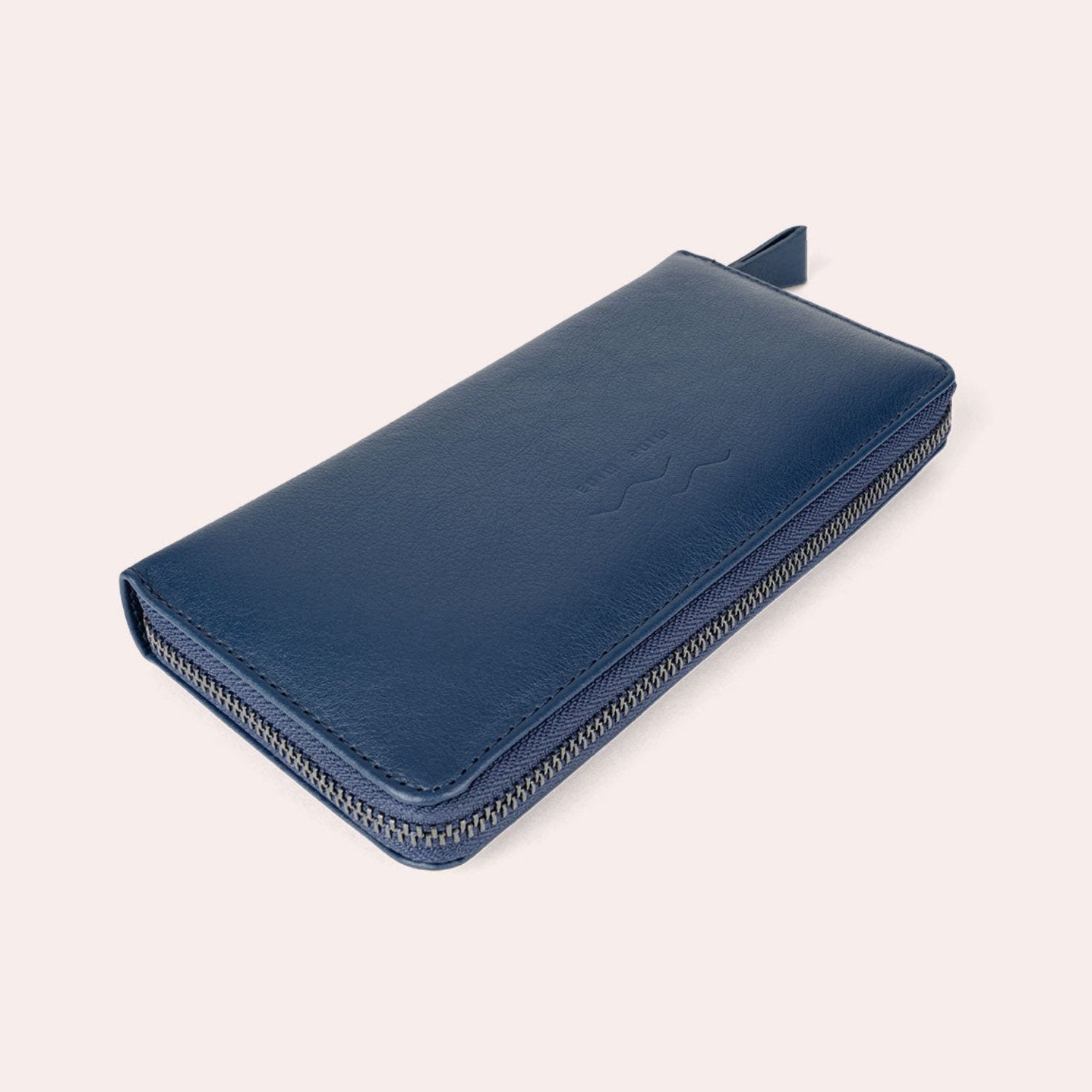 Eine blaue Ledergeldbörse mit Reißverschluss ist auf einem hellen Hintergrund abgebildet. Das Portemonnaie ist geschlossen, mit einem Reißverschluss entlang der Kante und einer kleinen Zuglasche sichtbar.