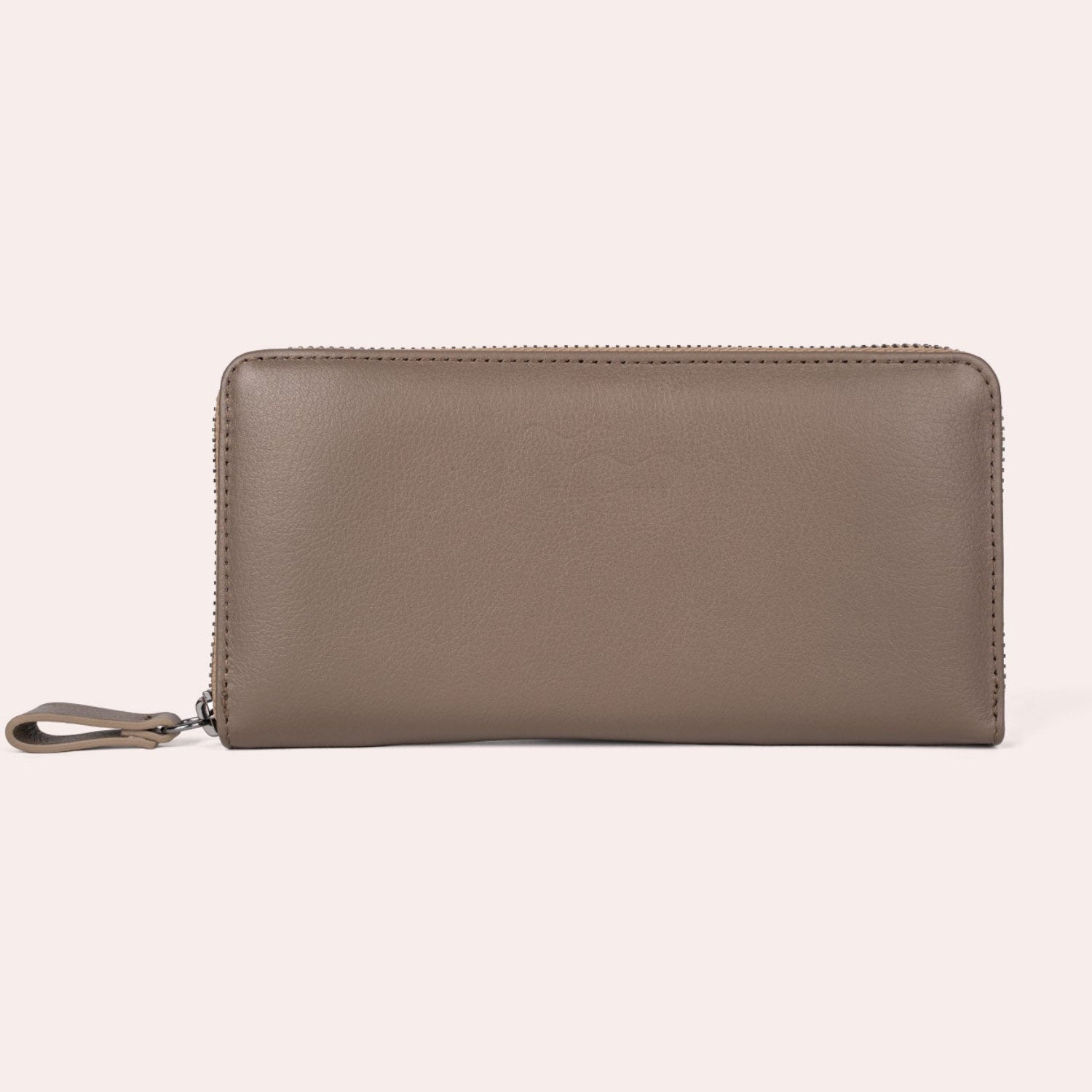Ein taupefarbenes Lederportemonnaie mit Reißverschluss und Handschlaufe vor einem schlichten hellen Hintergrund.