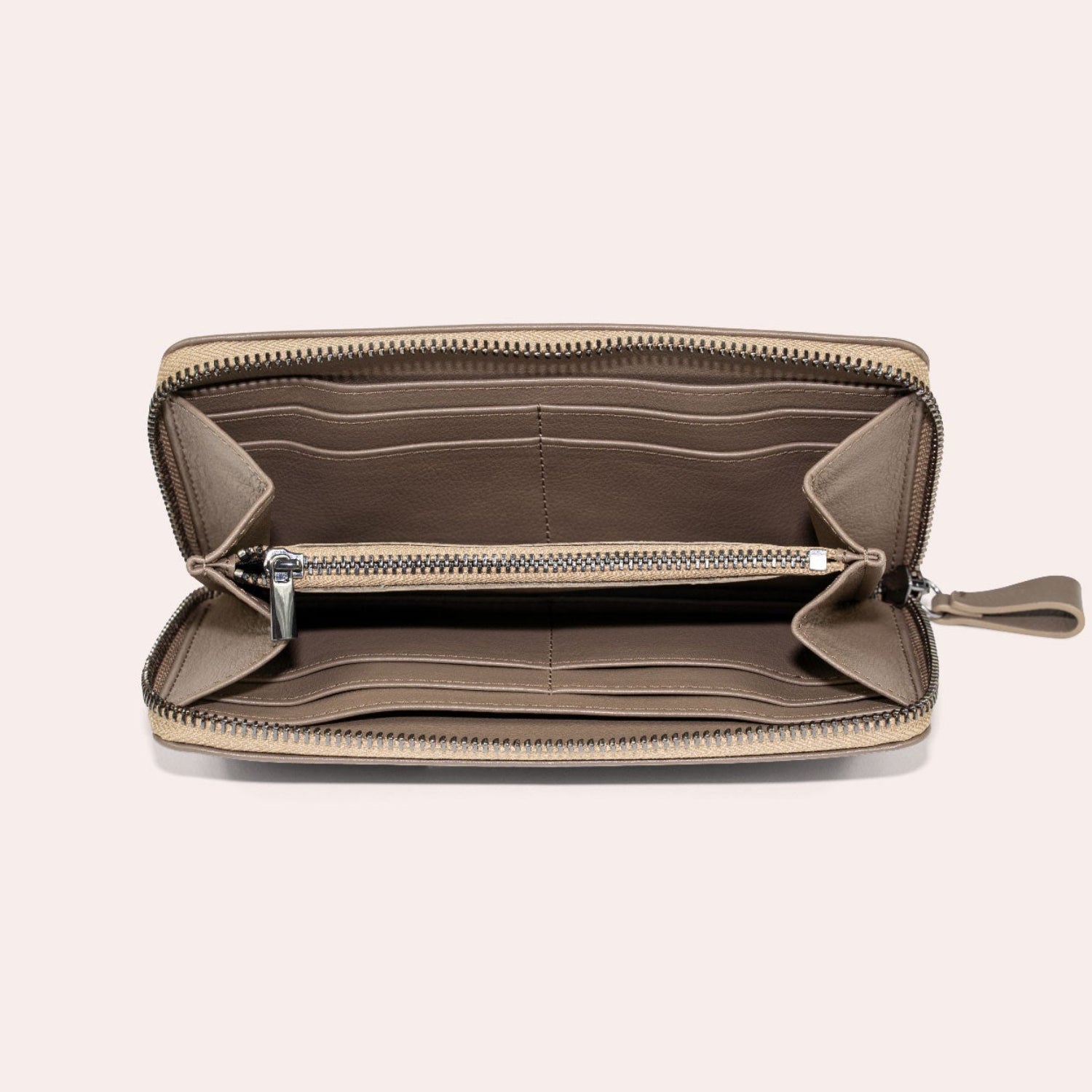 Ein taupefarbenes Portemonnaie mit Reißverschluss ist geöffnet und zeigt mehrere Kartenfächer, ein Münzfach mit Reißverschluss in der Mitte und leere Fächer, die sich alle vor einem hellen Hintergrund befinden.