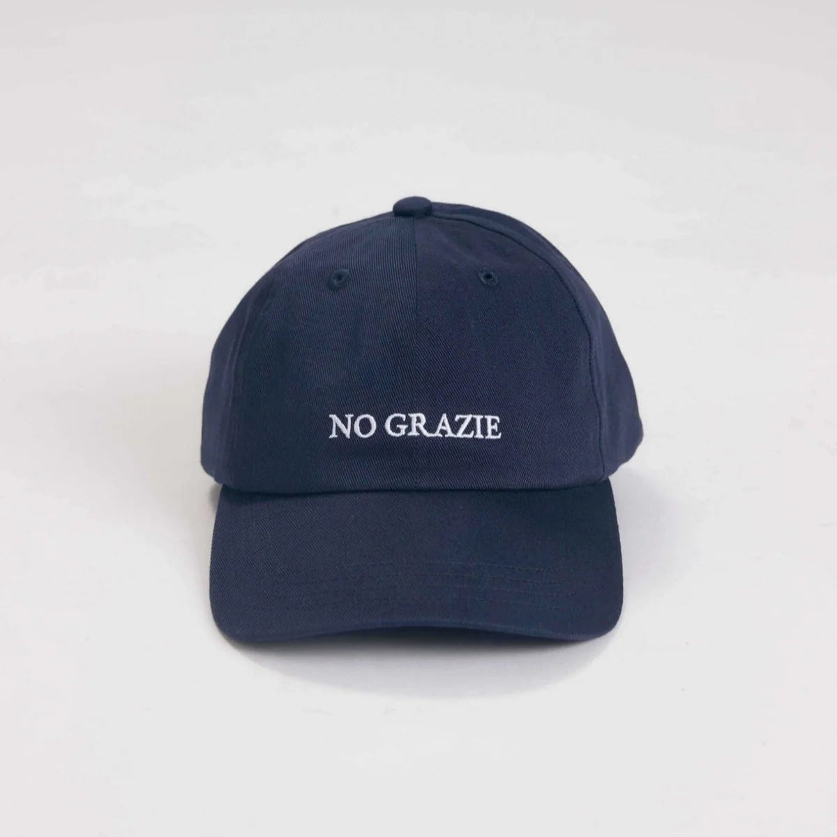 Eine marineblaue Baseballkappe mit dem in weißer Farbe aufgestickten Schriftzug NO GRAZIE auf der Vorderseite, der auf einem schlichten weißen Hintergrund abgebildet ist.