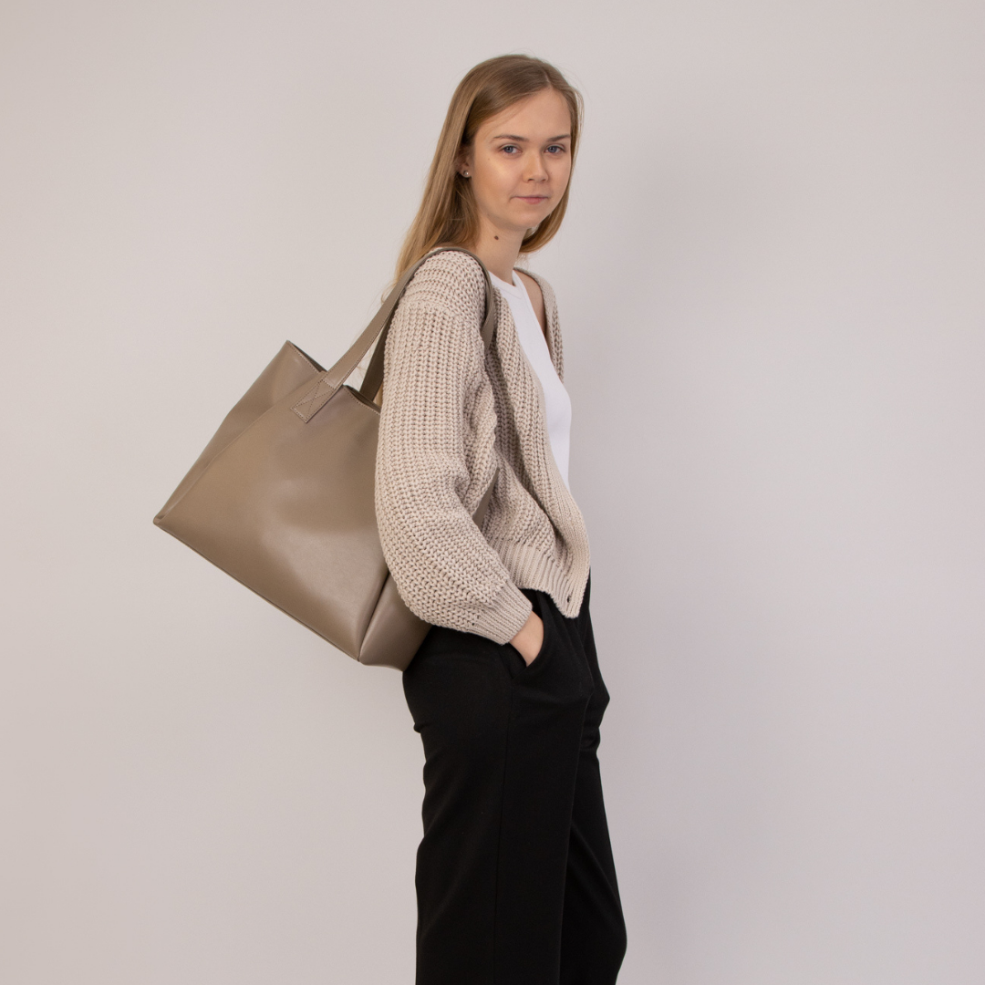 Eine Frau in hellem Pullover trägt eine große, beige Tasche über der Schulter und blickt zur Seite.