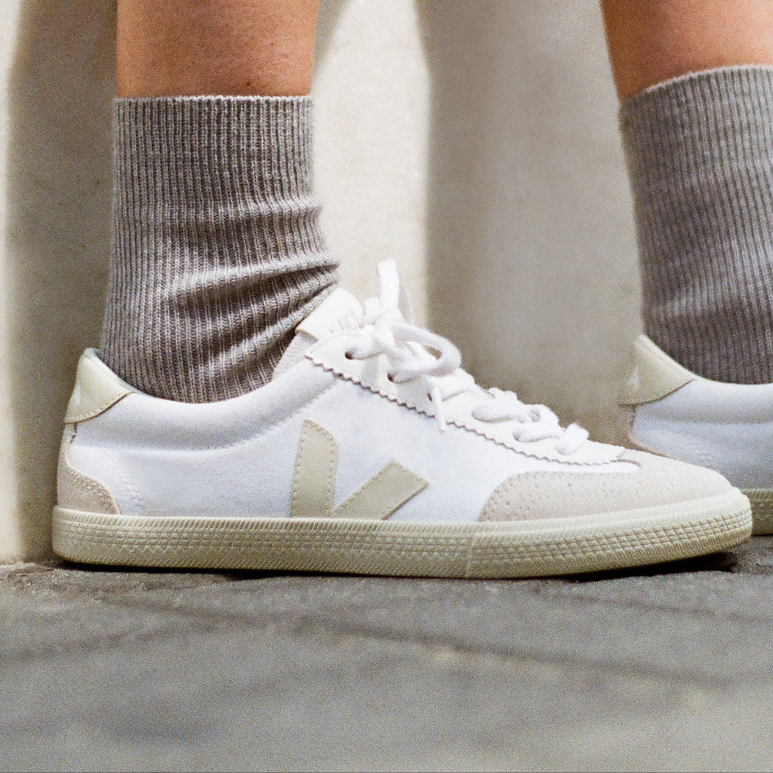 Nahaufnahme von zwei Füßen in weißen Turnschuhen und grauen Socken auf einem Betonboden.