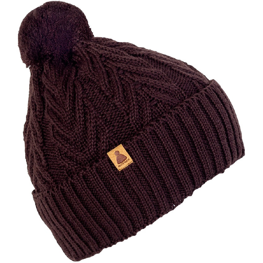 Eine dunkelbraune Strickmütze mit umgeschlagener Krempe, einem kleinen Lederaufnäher und einem Bommel an der Spitze vor weißem Hintergrund.