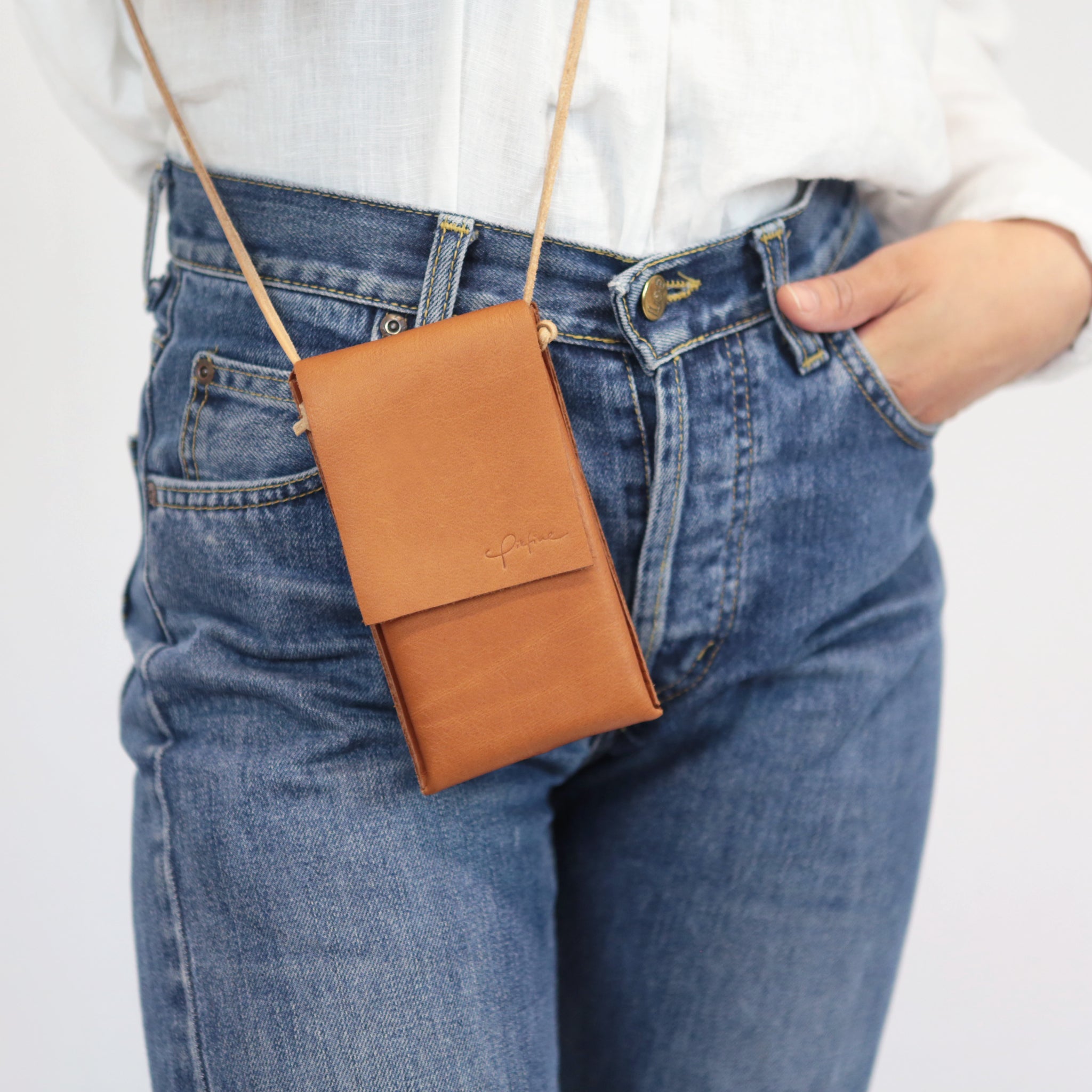 Person mit blauer Jeans und weißem Hemd trägt eine braune Leder-Umhängetasche.