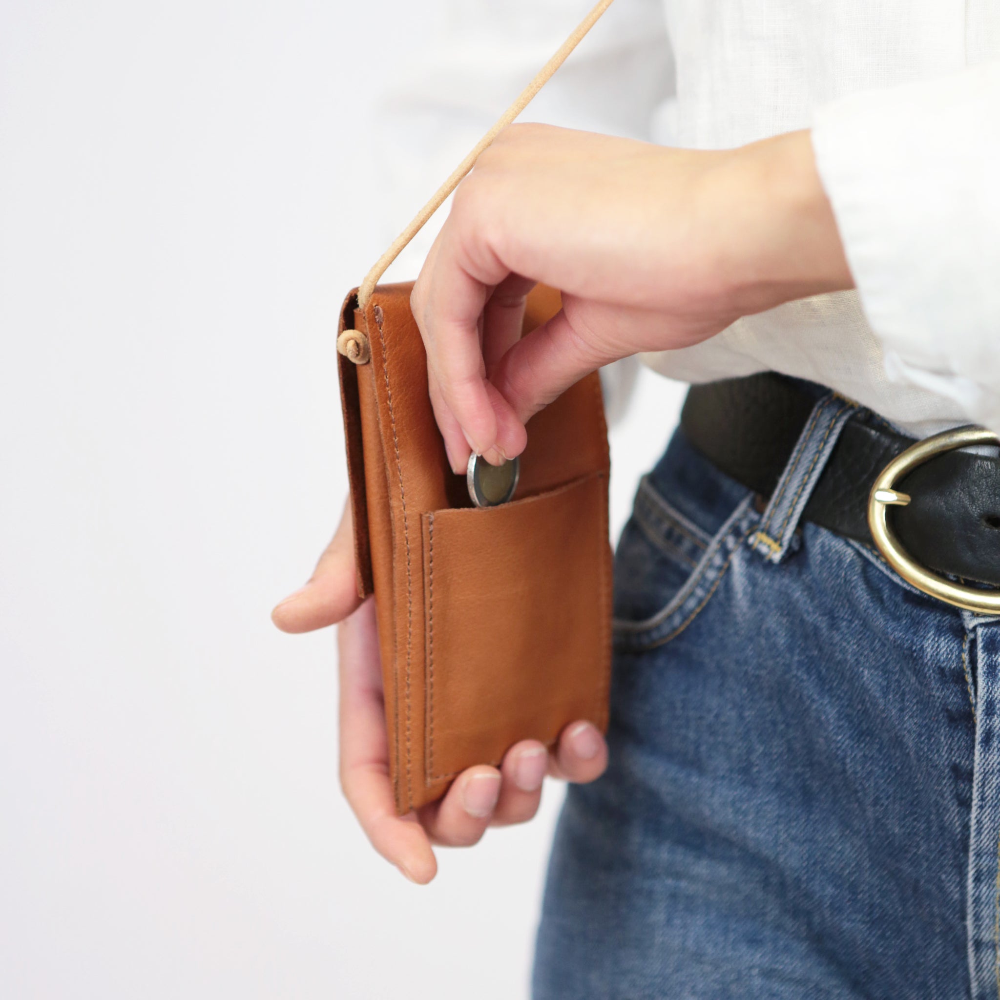 Person steckt eine Münze in eine braune Ledertasche, die um den Hals hängt.