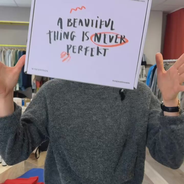 Person hält ein Schild mit der Aufschrift "A beautiful thing is never perfect" hoch; Hintergrund aus Kleidung.