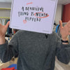 Person hält ein Schild mit der Aufschrift "A beautiful thing is never perfect" hoch; Hintergrund aus Kleidung.