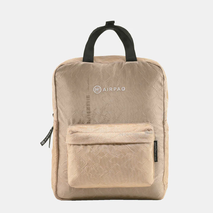 Ein beiger, quadratischer Rucksack mit schwarzen Griffen, einer Vordertasche mit Reißverschluss und dem AIRPAQ-Logo auf der oberen Vorderseite vor einem schlichten weißen Hintergrund.