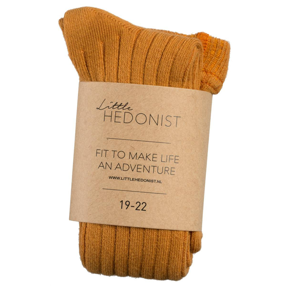 Ein Paar gefaltete senfgelbe Rippensocken, eingewickelt in ein braunes Papieretikett mit der Aufschrift Little Hedonist, Fit to make life an adventure, 19-22.