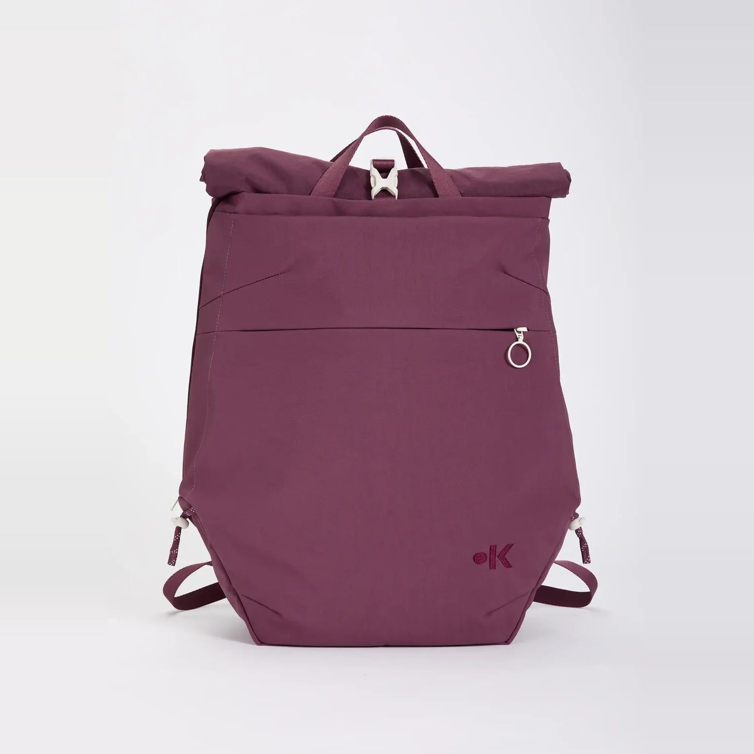 Violetter Rolltop-Rucksack mit einer Reißverschlusstasche auf der Vorderseite, einem Metallverschluss an der Oberseite, seitlichen Riemen und einem kleinen runden Logo in der rechten unteren Ecke.
