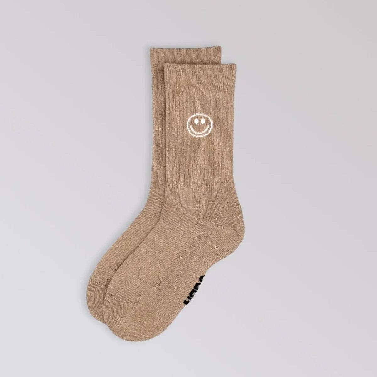 Ein Paar beigefarbene Socken mit einem weißen Smiley-Motiv am oberen Rand auf hellgrauem Hintergrund.