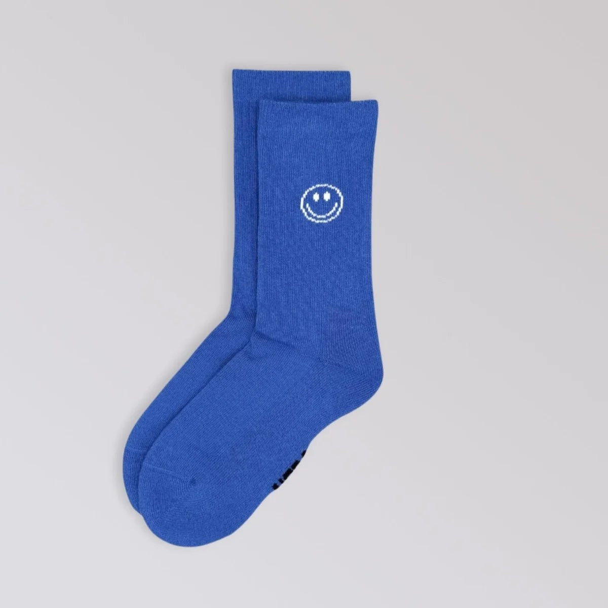 Ein Paar blaue Socken mit einem kleinen weißen Smiley-Motiv am oberen Rand auf hellgrauem Hintergrund.