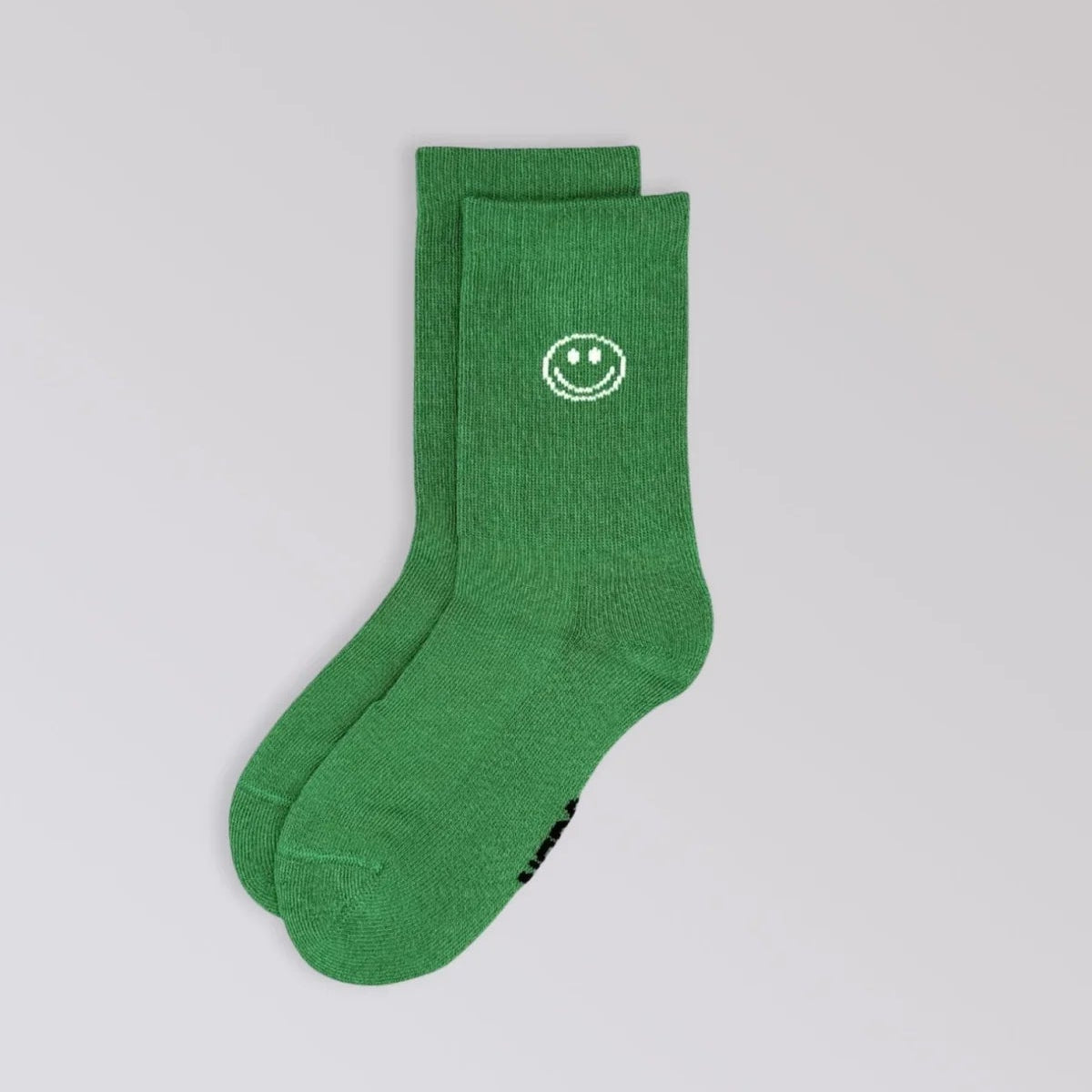 Ein Paar grüne Socken mit einem weißen Smiley-Motiv im oberen Bereich auf einem schlichten hellgrauen Hintergrund.
