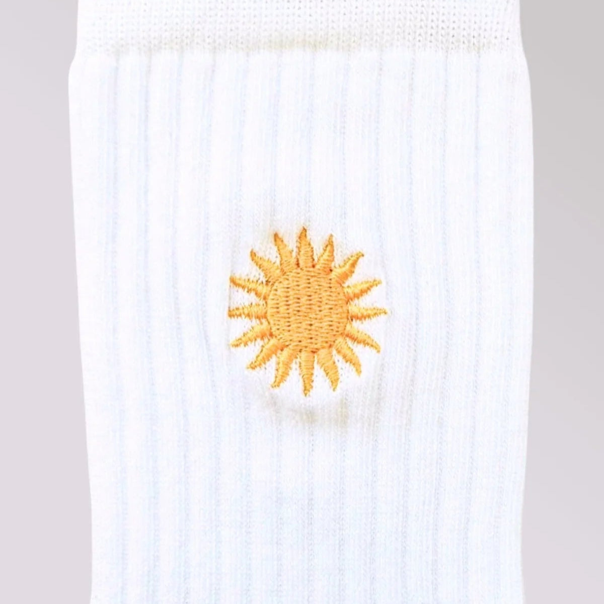 Nahaufnahme einer weißen gerippten Socke mit einem kleinen, gestickten gelben Sonnenmotiv in der Mitte.
