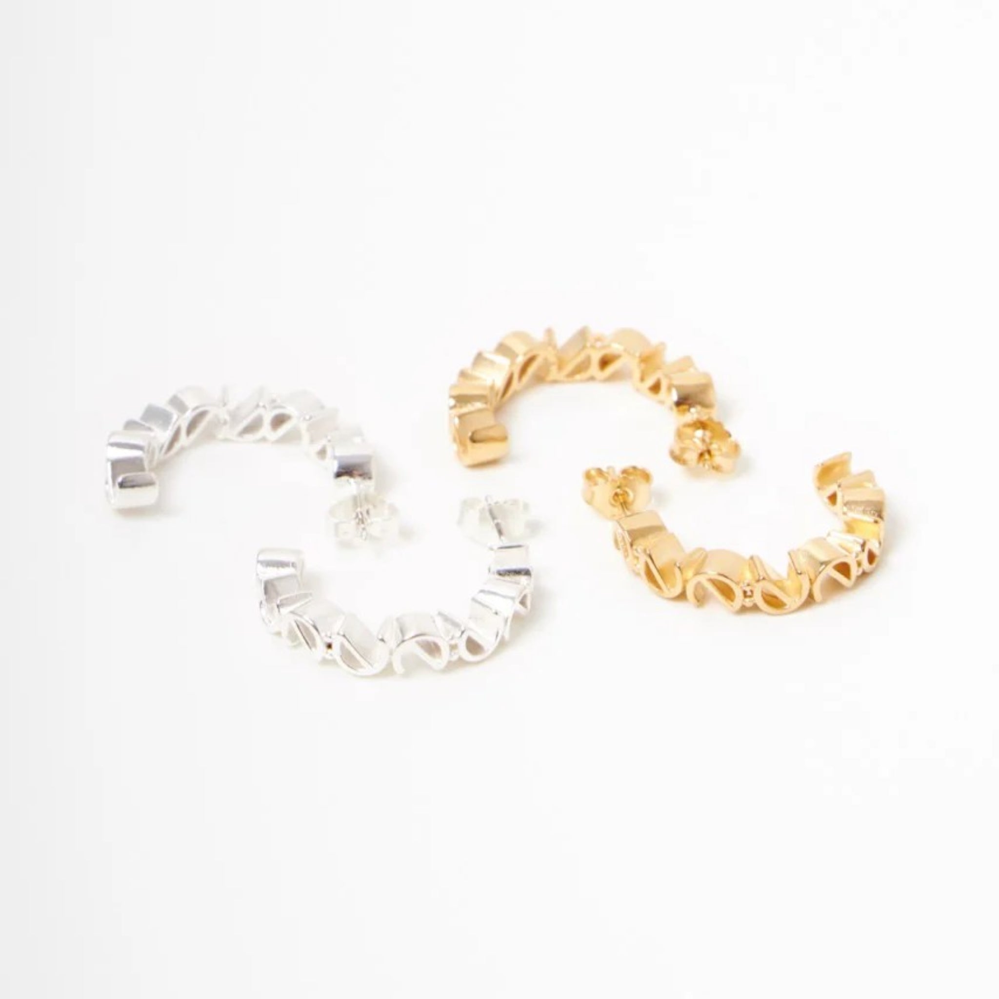 Silberne und goldene Creolen mit geschwungenem Design auf weißem Hintergrund.