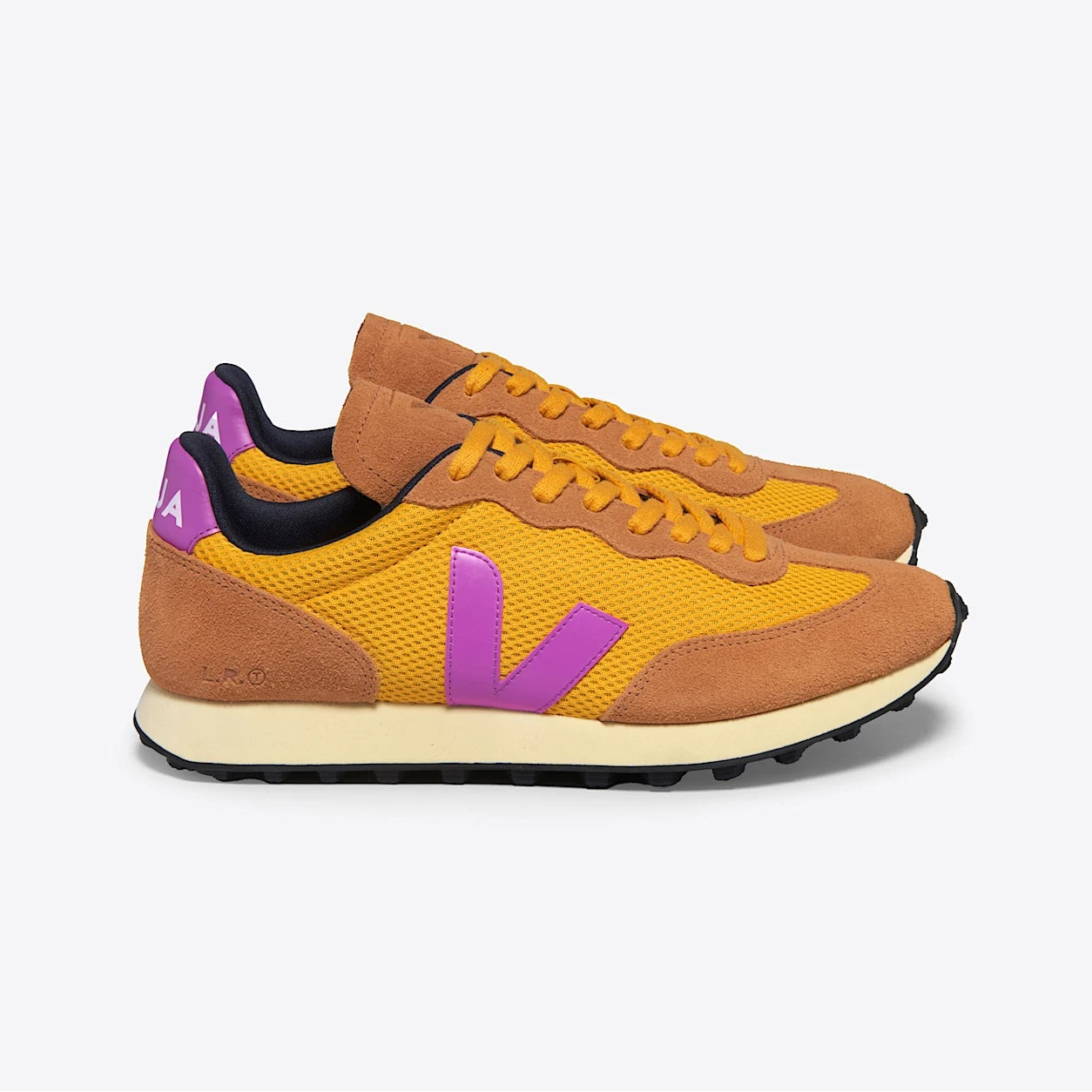 Ein Paar Turnschuhe mit braunem Wildleder, gelben Mesh-Einsätzen, violetten "V"-Logos an den Seiten, violetten Fersenakzenten und cremefarbenen Sohlen, die vor einem schlichten weißen Hintergrund stehen.