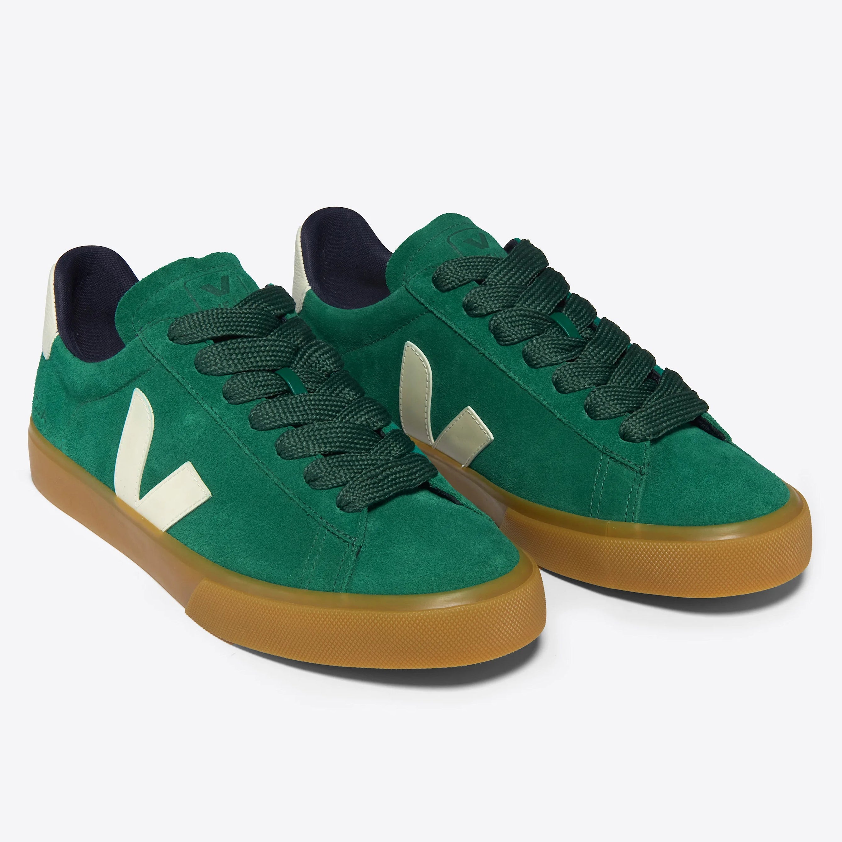 Ein Paar grüne Wildleder-Turnschuhe mit dicken dunkelgrünen Schnürsenkeln, beigen Gummisohlen und einem cremefarbenen V-Logo an den Seiten auf einem schlichten hellgrauen Hintergrund.