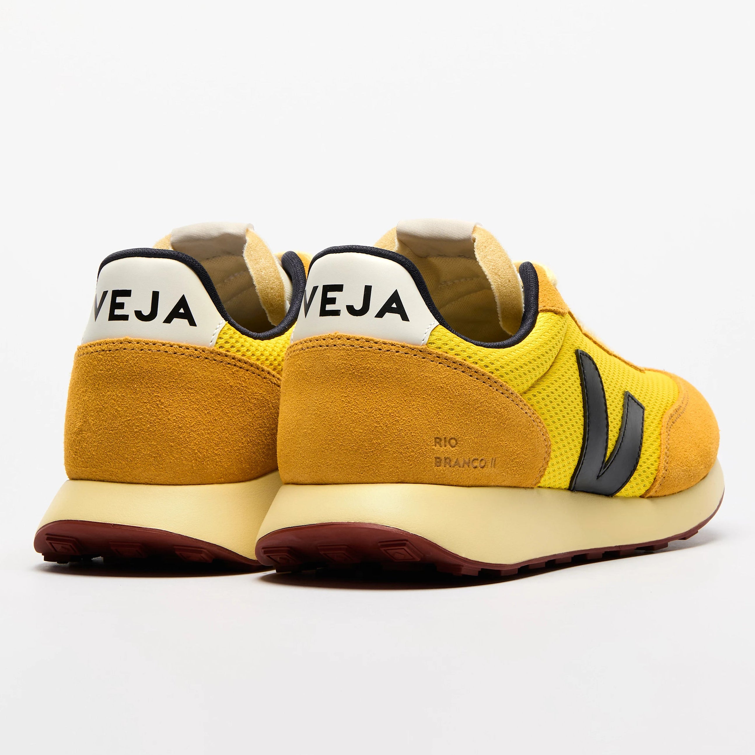 Ein Paar gelbe Veja-Sneakers mit schwarzen Details und dem Markennamen VEJA auf den weißen Fersenlaschen auf weißem Hintergrund.