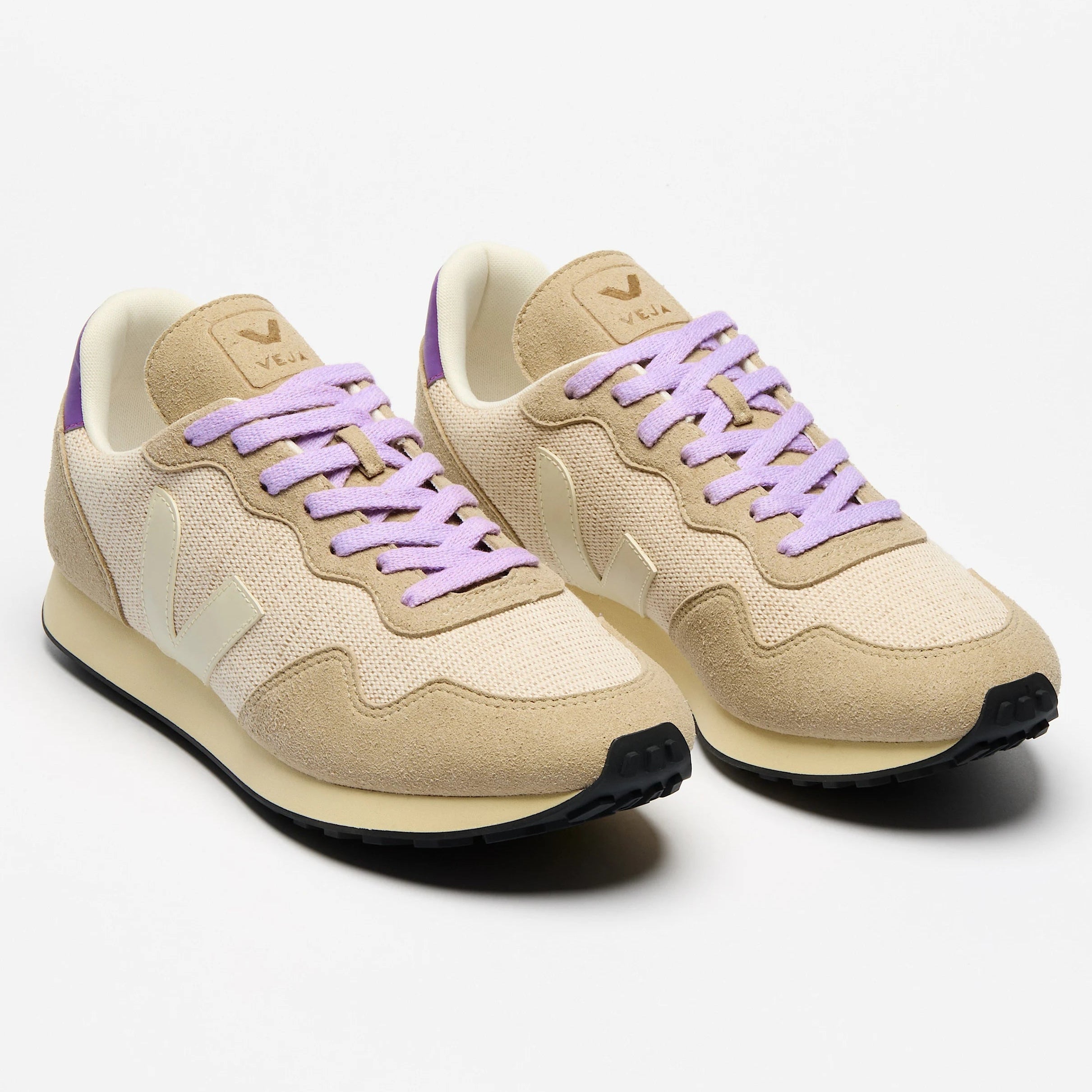 Ein Paar beigefarbene Turnschuhe mit lilafarbenen Schnürsenkeln, weißen V-Logos an den Seiten und schwarzen Sohlen auf weißem Hintergrund.
