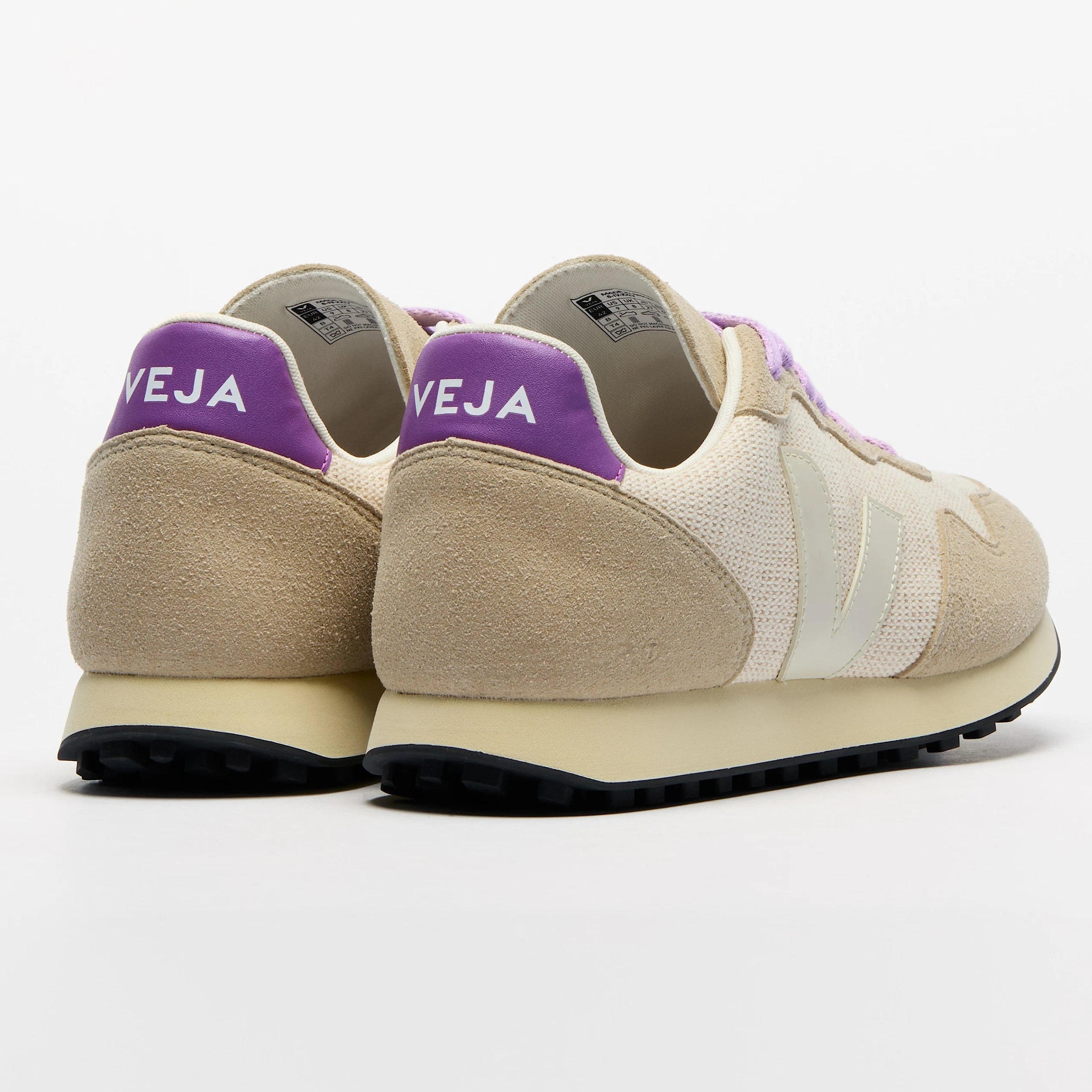 Ein Paar beige-weiße Turnschuhe mit lilafarbenen Fersenlaschen, auf denen der Markenname VEJA steht, nebeneinander auf einem schlichten weißen Hintergrund, von hinten gesehen.