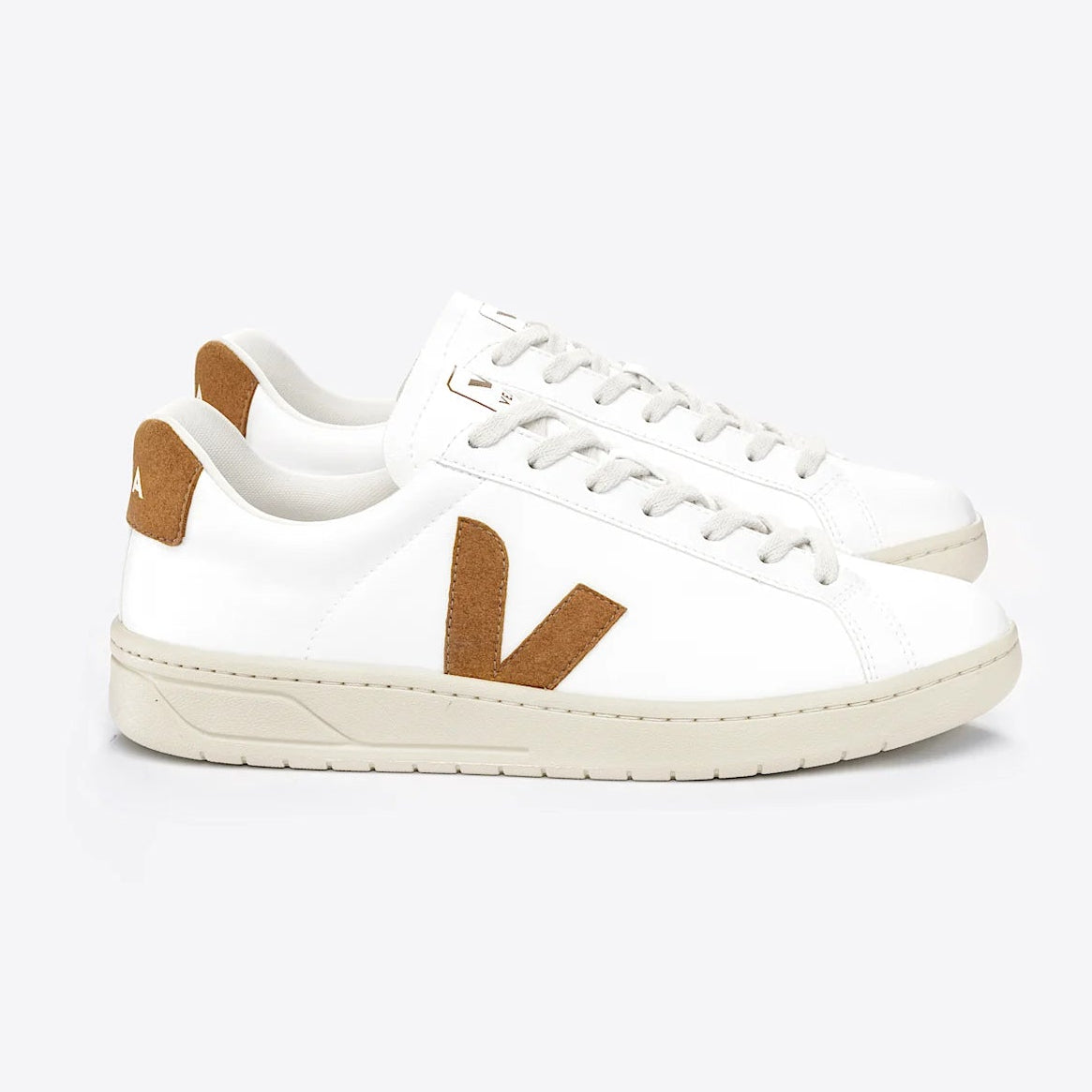 Ein Paar weißer Turnschuhe mit beiger Sohle und hellbraunen Wildlederdetails, einschließlich eines großen V an der Seite und Akzenten an der Ferse, vor einem einfarbigen hellgrauen Hintergrund.