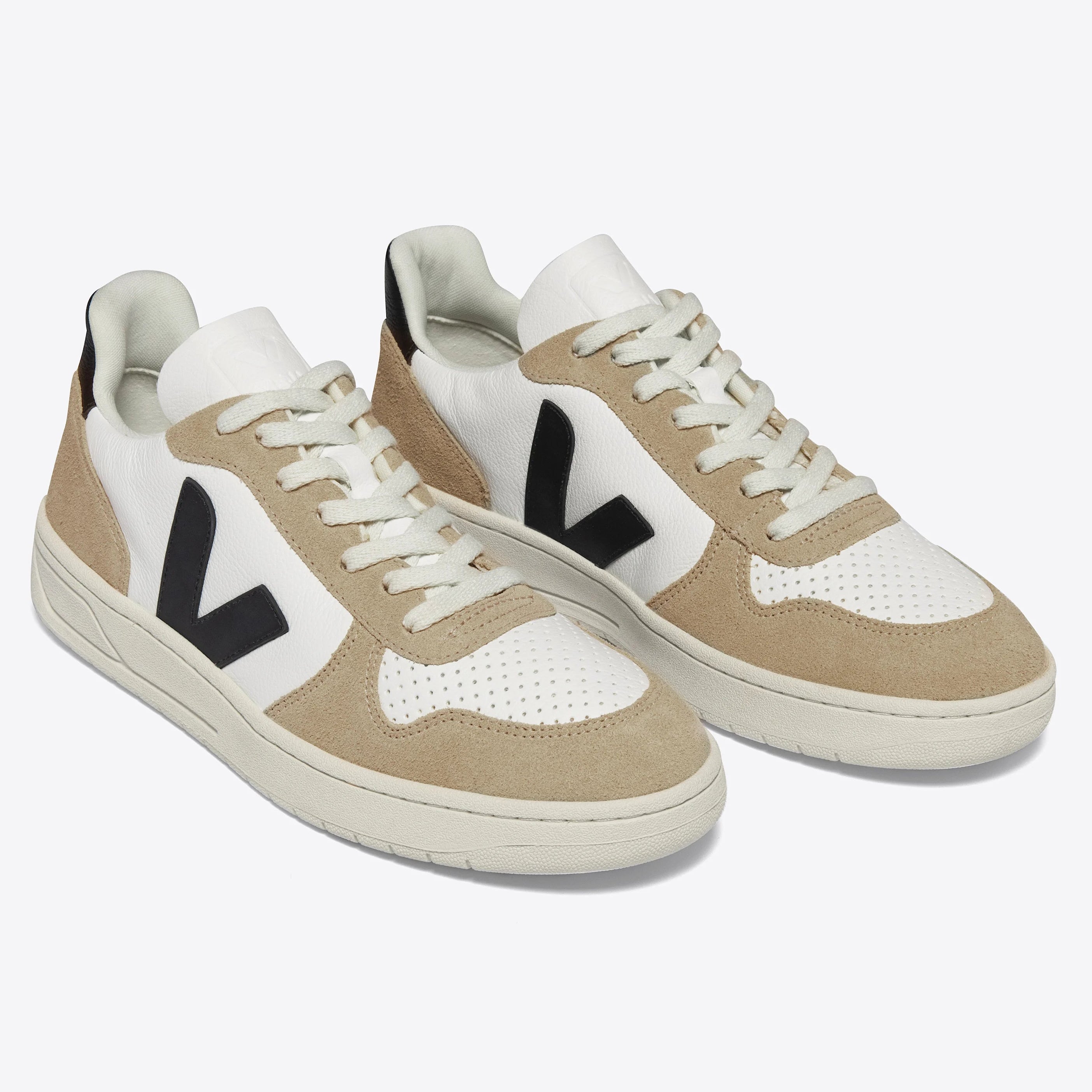 Ein Paar weiß-beigefarbene Sneaker mit schwarzem V-Logo an den Seiten, weißen Schnürsenkeln und perforierten Details an den Zehenkappen auf einem schlichten hellen Hintergrund.