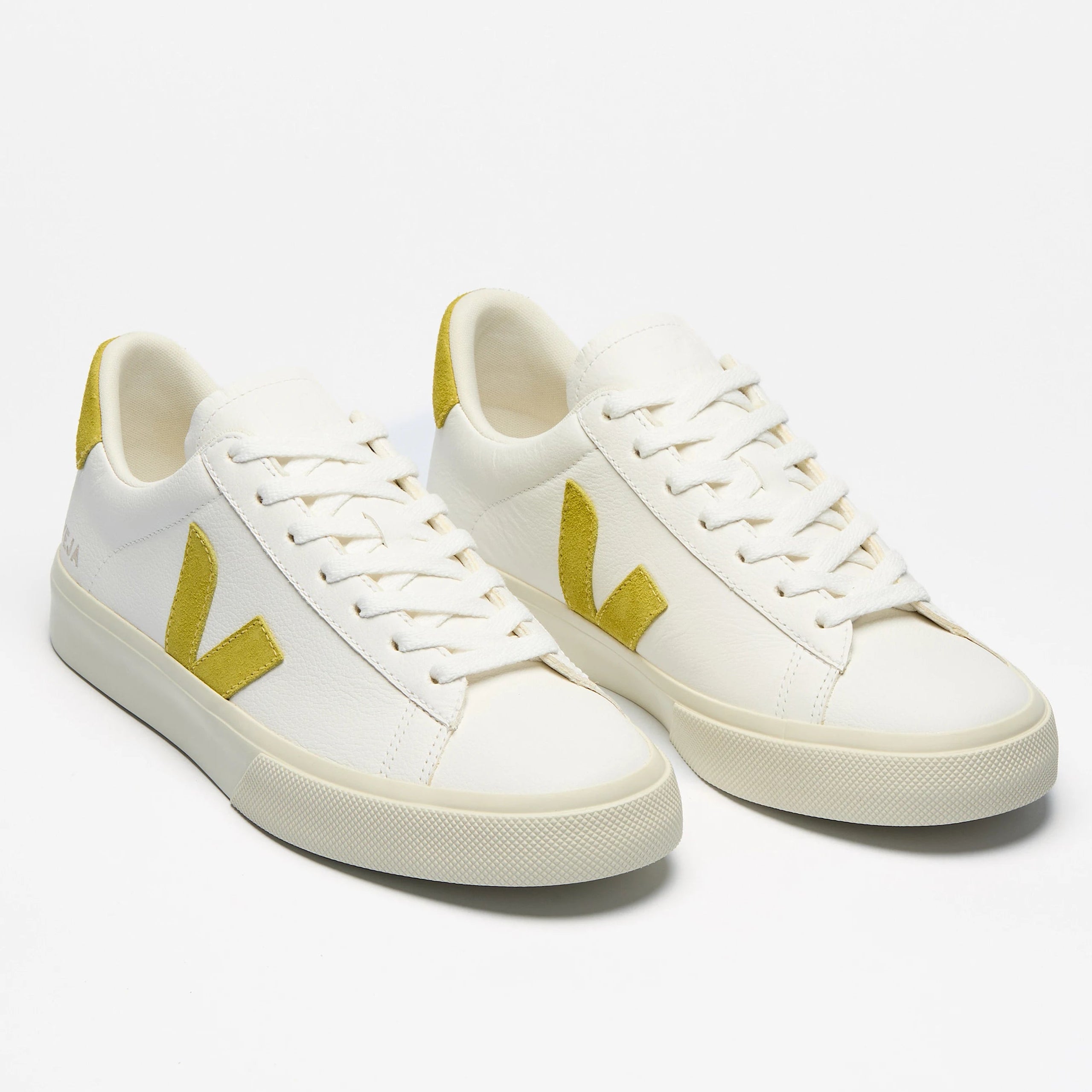 Ein Paar weiße Turnschuhe mit gelben Akzenten an der Ferse und dem seitlichen Logo auf einem schlichten weißen Hintergrund.