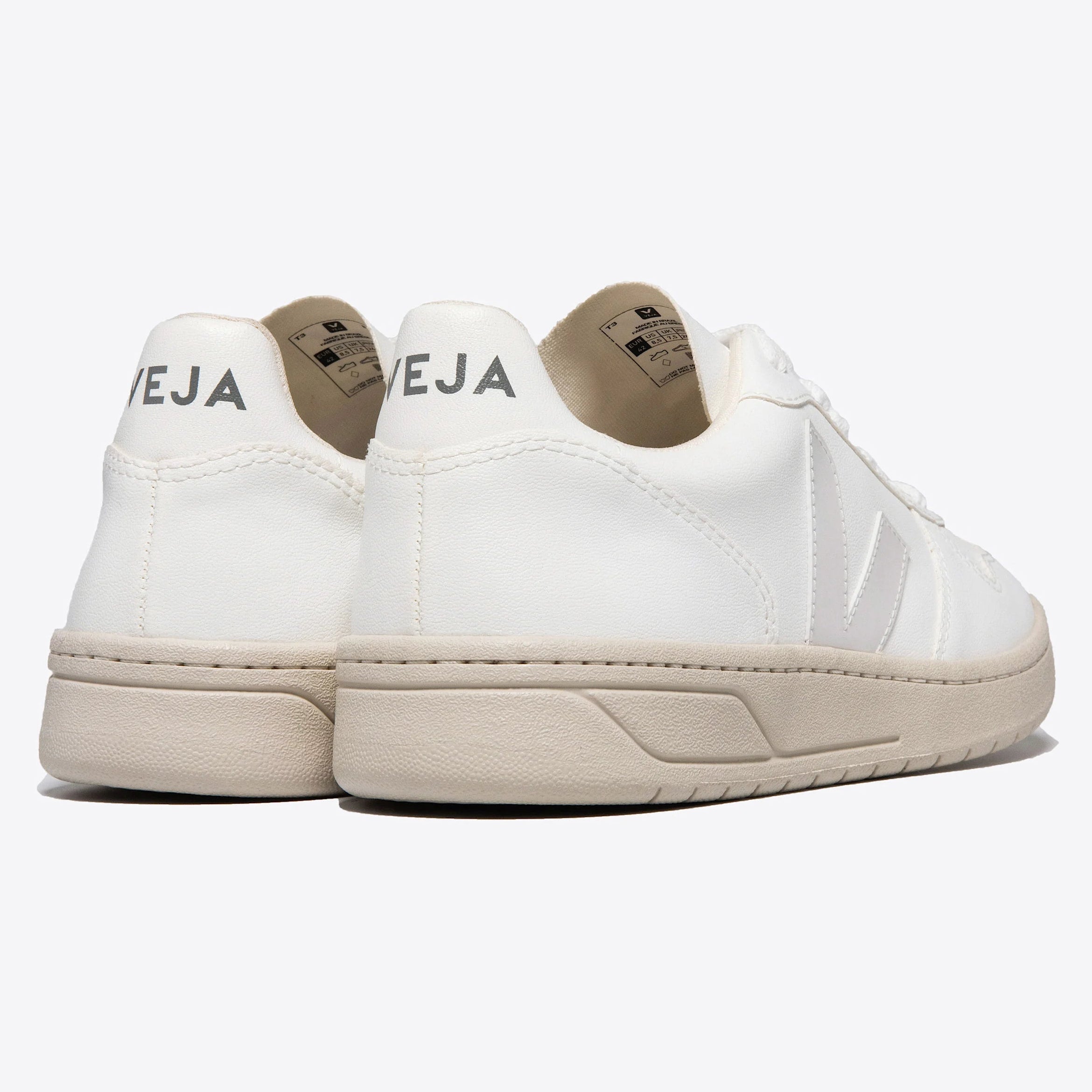 Ein Paar weiße Veja-Turnschuhe mit beiger Sohle, von hinten und von der Seite gesehen, mit dem Markennamen VEJA an den Fersen.