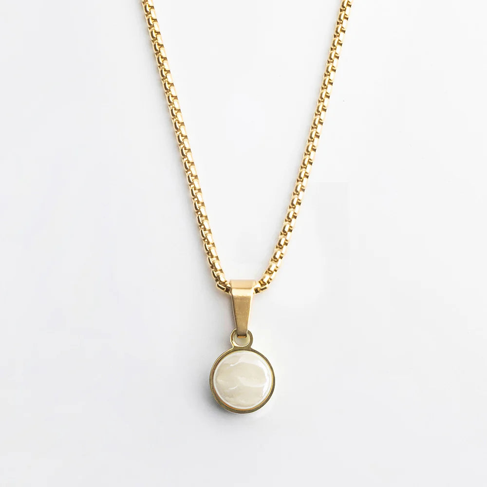 Goldkette mit einem runden weißen Anhänger in einer goldenen Lünette, der vor einem schlichten weißen Hintergrund steht.
