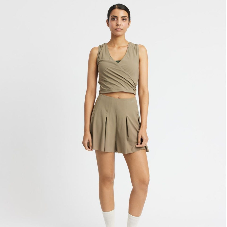 Frau in einem beigefarbenen, ärmellosen Top und passenden Shorts vor weißem Hintergrund.