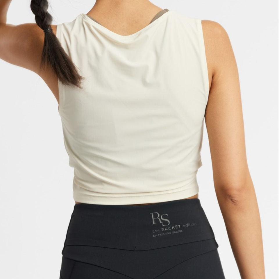 Frau in heller Sportbekleidung von hinten, trägt schwarzes RS-Logo auf Capri-Leggings, langes Haar in Zopf geflochten.