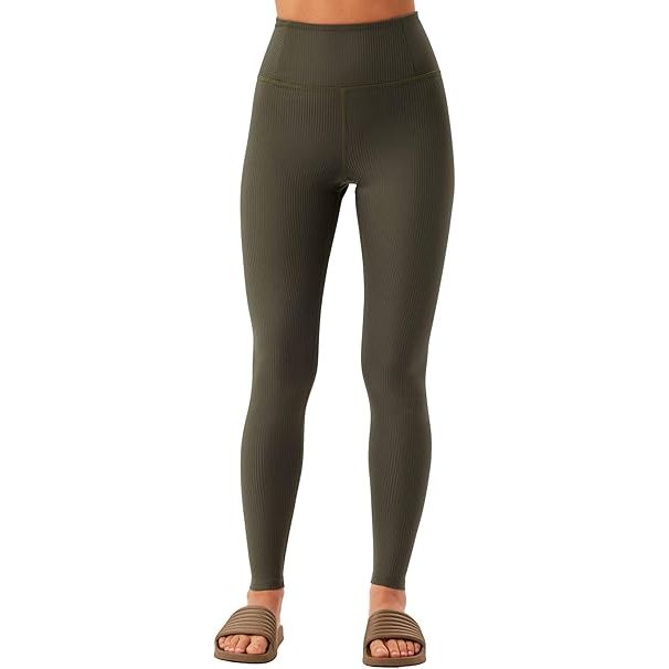 Eine Person, die hochtaillierte, gerippte olivgrüne Leggings und braune Gleitsandalen trägt, steht vor einem weißen Hintergrund. Der Oberkörper der Person ist nicht sichtbar.