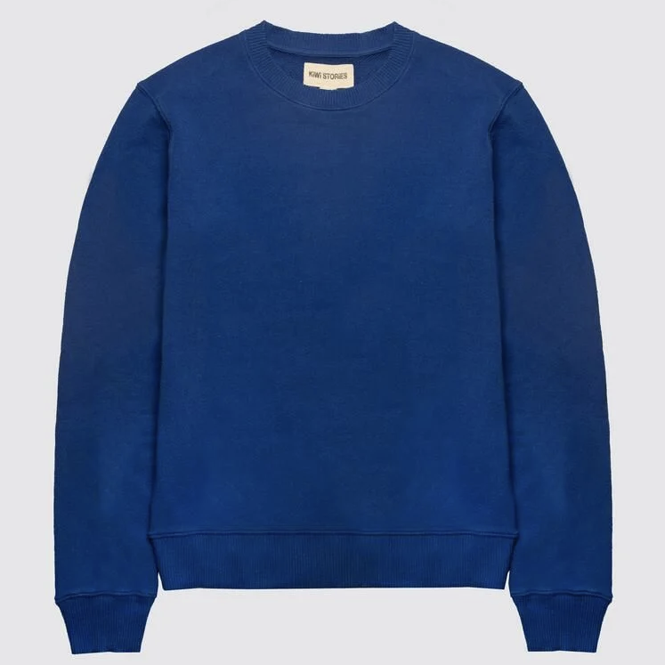 Ein einfarbiges blaues Sweatshirt mit Rundhalsausschnitt und langen Ärmeln liegt flach auf einem hellgrauen Hintergrund.