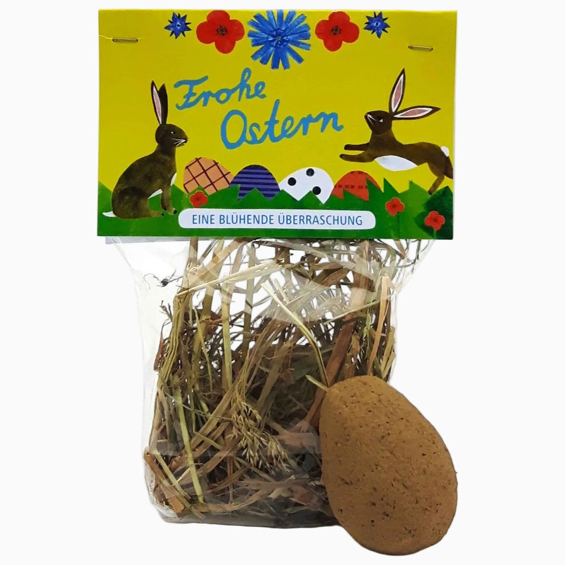 Eine Verpackung mit Stroh, einem eiförmigen Gegenstand und einem gelben Etikett mit Hasen, verzierten Eiern, Blumen und dem deutschen Text Frohe Ostern und eine blühende Überraschung.
