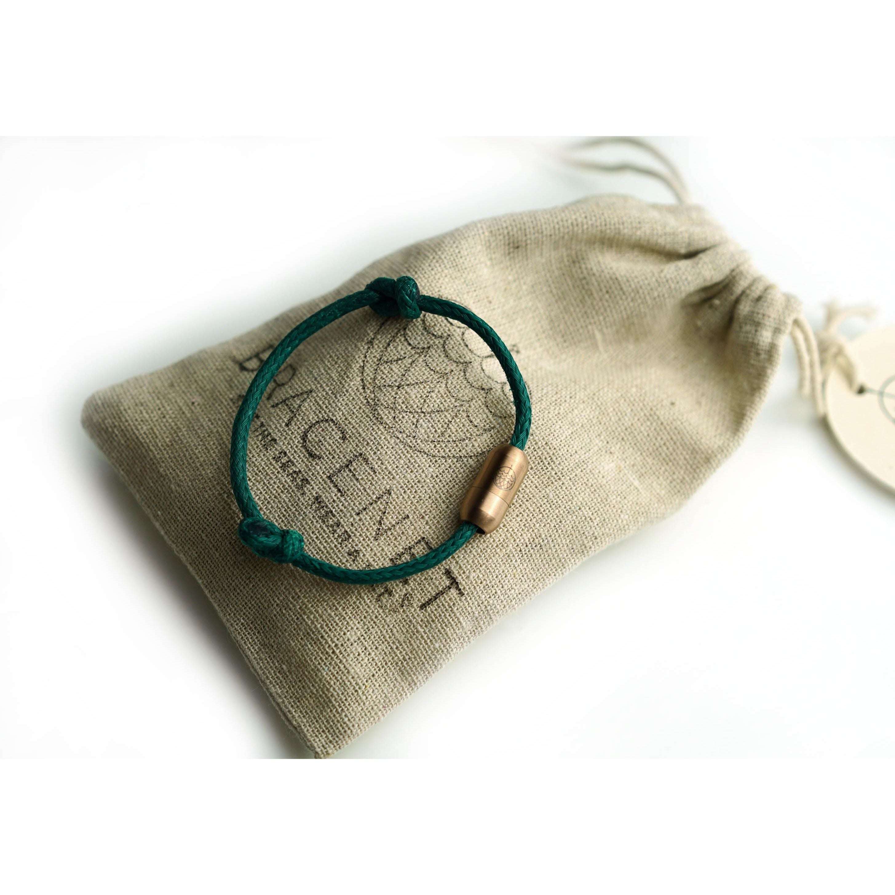 Ein grünes Armband mit einem bronzefarbenen Verschluss liegt auf einem beigen Stoffbeutel mit Aufdruck.