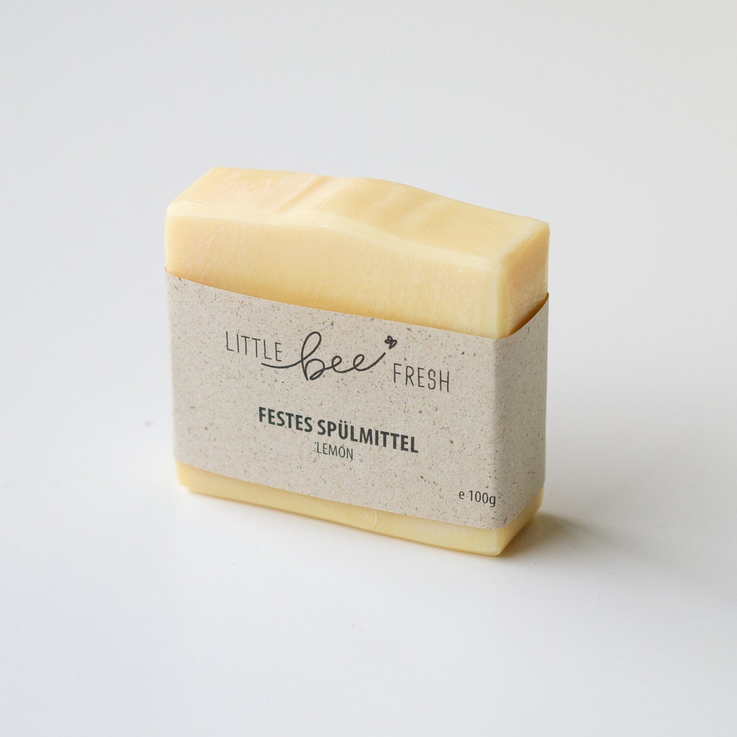 Ein gelbes Stück festes Spülmittel mit Etikett "Little Bee Fresh" und "Lemon" liegt auf einem weißen Hintergrund.