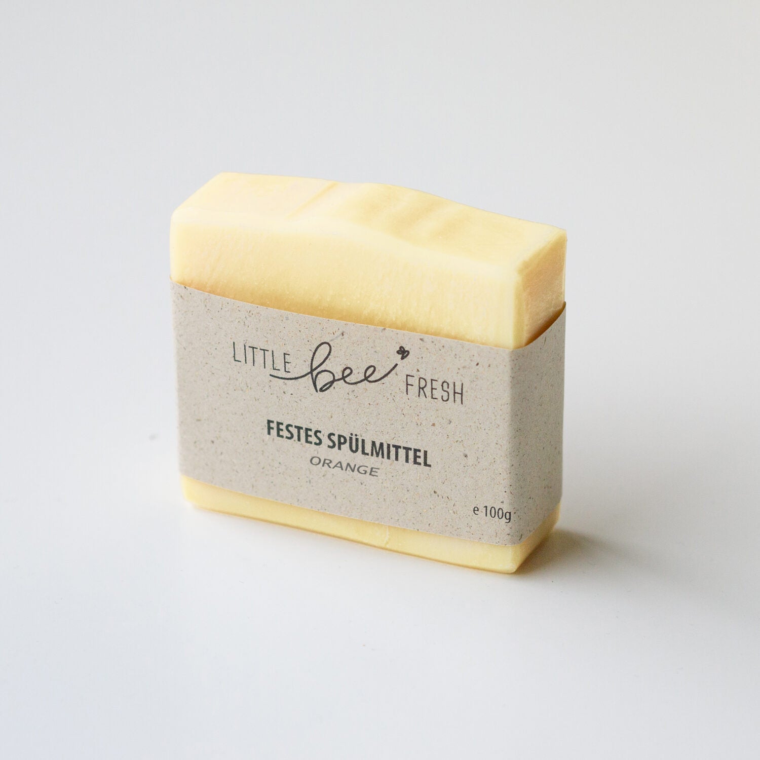 Ein festes gelbes Spülmittel mit Papierverpackung von "Little Bee Fresh" und der Aufschrift "FESTES SPÜLMITTEL ORANGE".