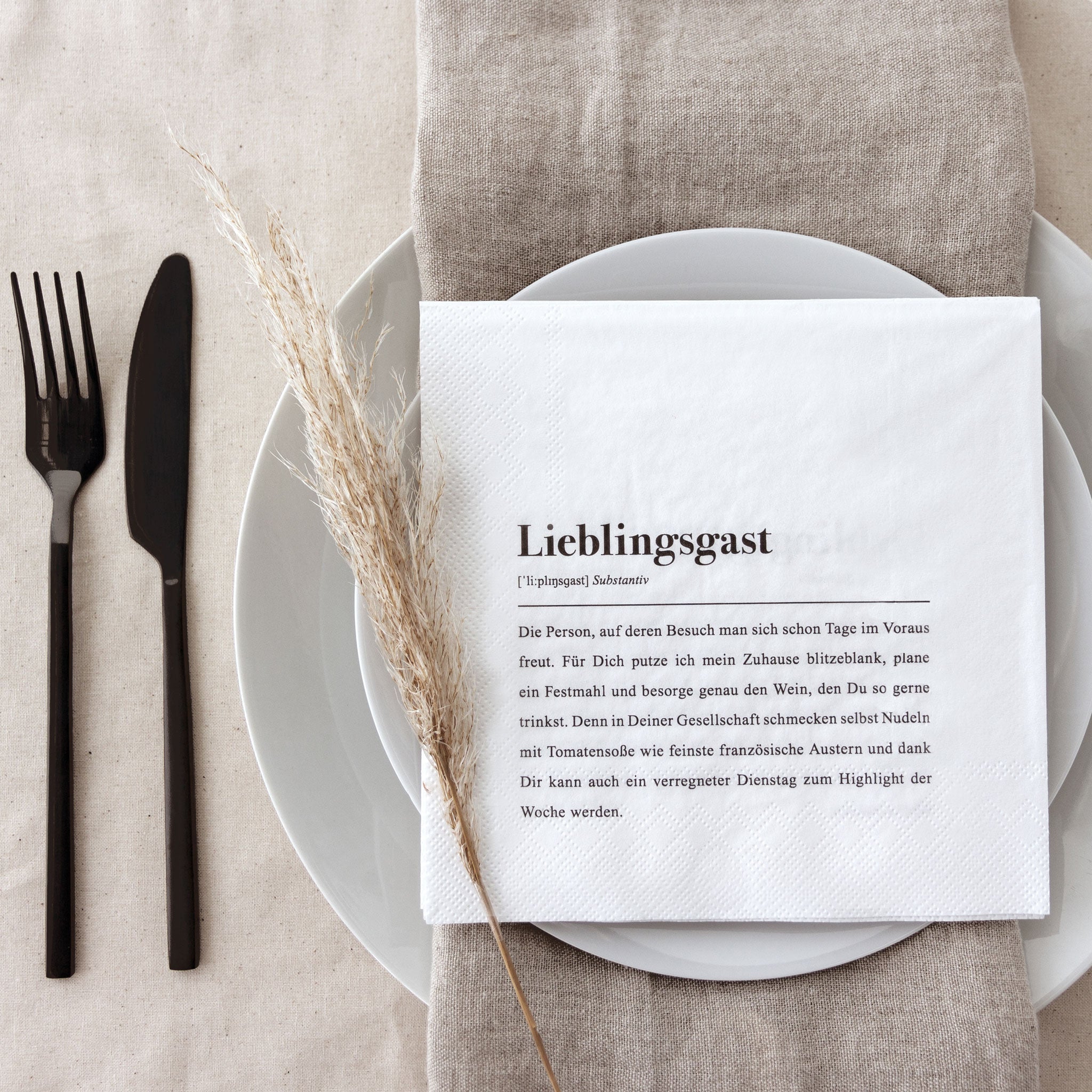 Ein gedeckter Tisch mit Besteck, einem Leinenserviette und einem Teller, auf dem eine dekorative Serviette liegt.