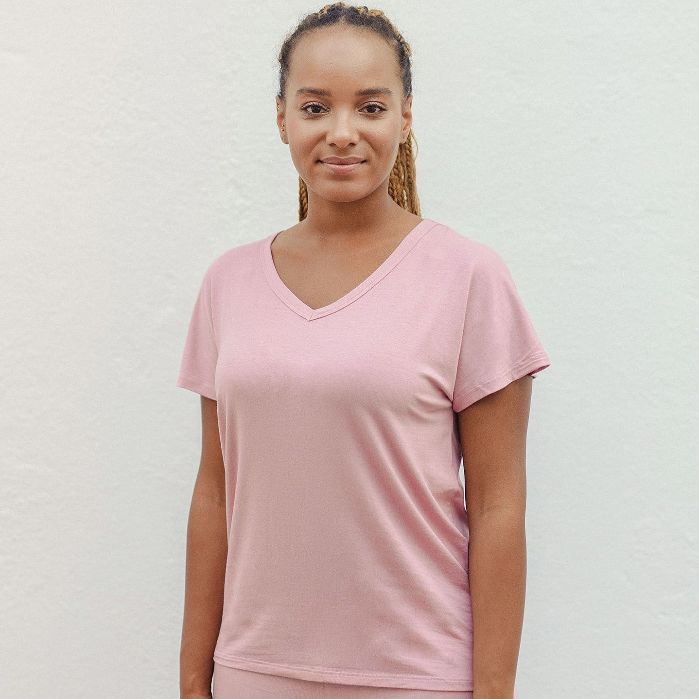 Eine Frau trägt ein rosafarbenes T-Shirt und steht vor einem hellen Hintergrund.