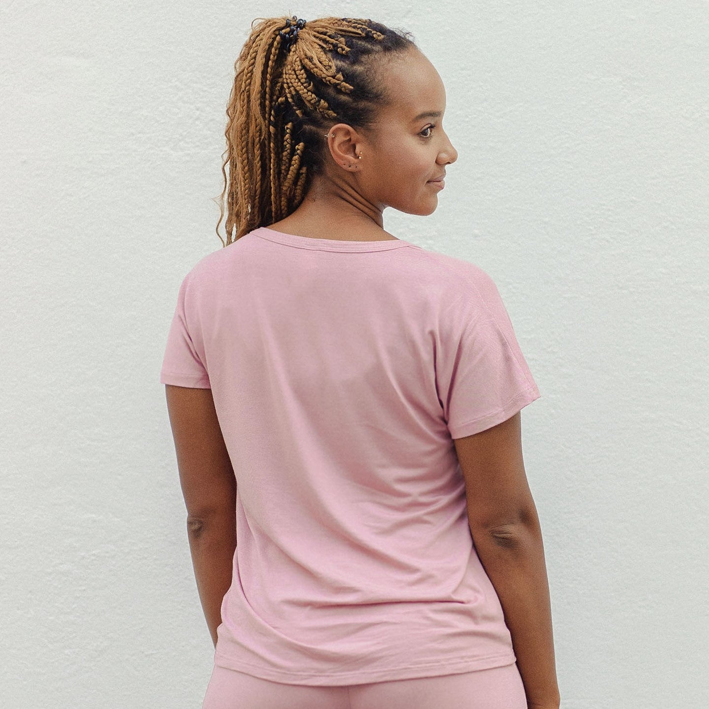 Eine Frau mit geflochtenem Haar trägt ein rosa T-Shirt und schaut von der Kamera weg.