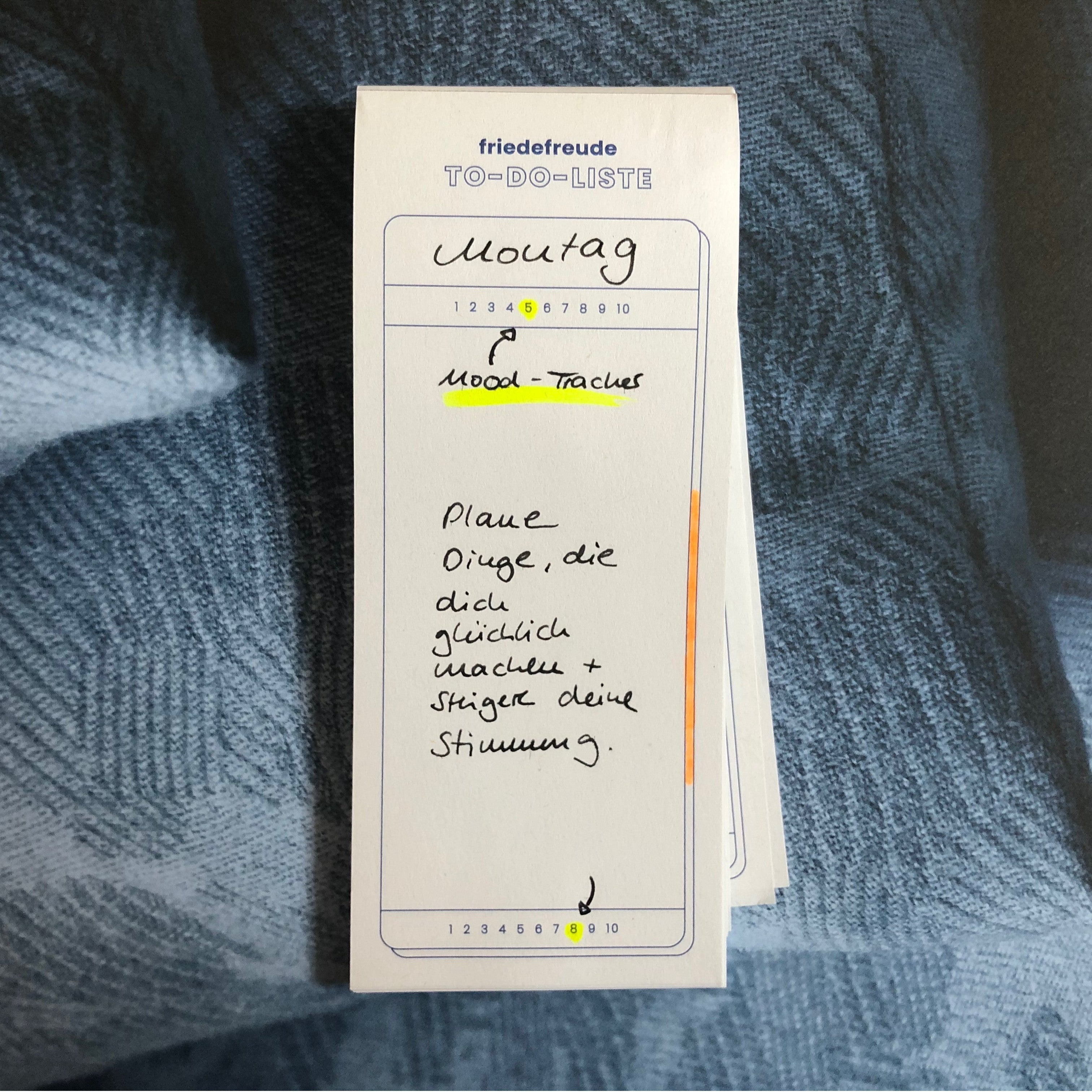 Notizblock mit der Überschrift "Montag" und handgeschriebener Notiz über das Planen von stimmungshebenden Aktivitäten.